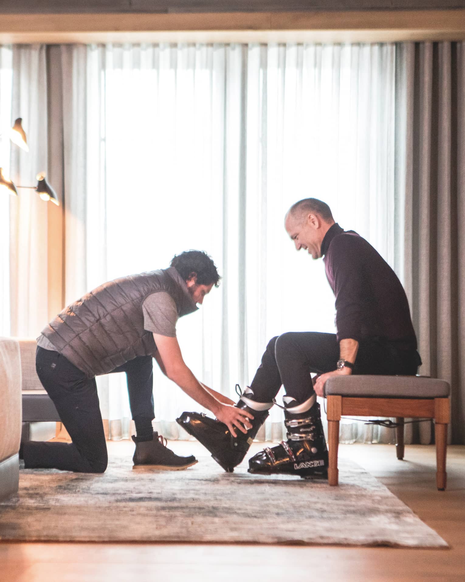 One man helping another to put on ski shoes.