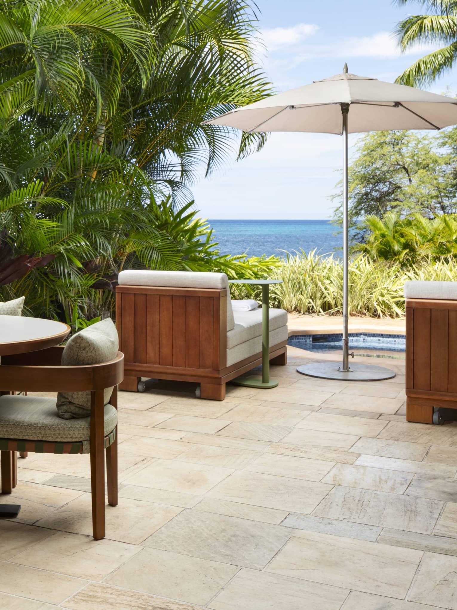 Private terrace with lush palm trees, dining table for four, two lounge chairs, spa tub and ocean view