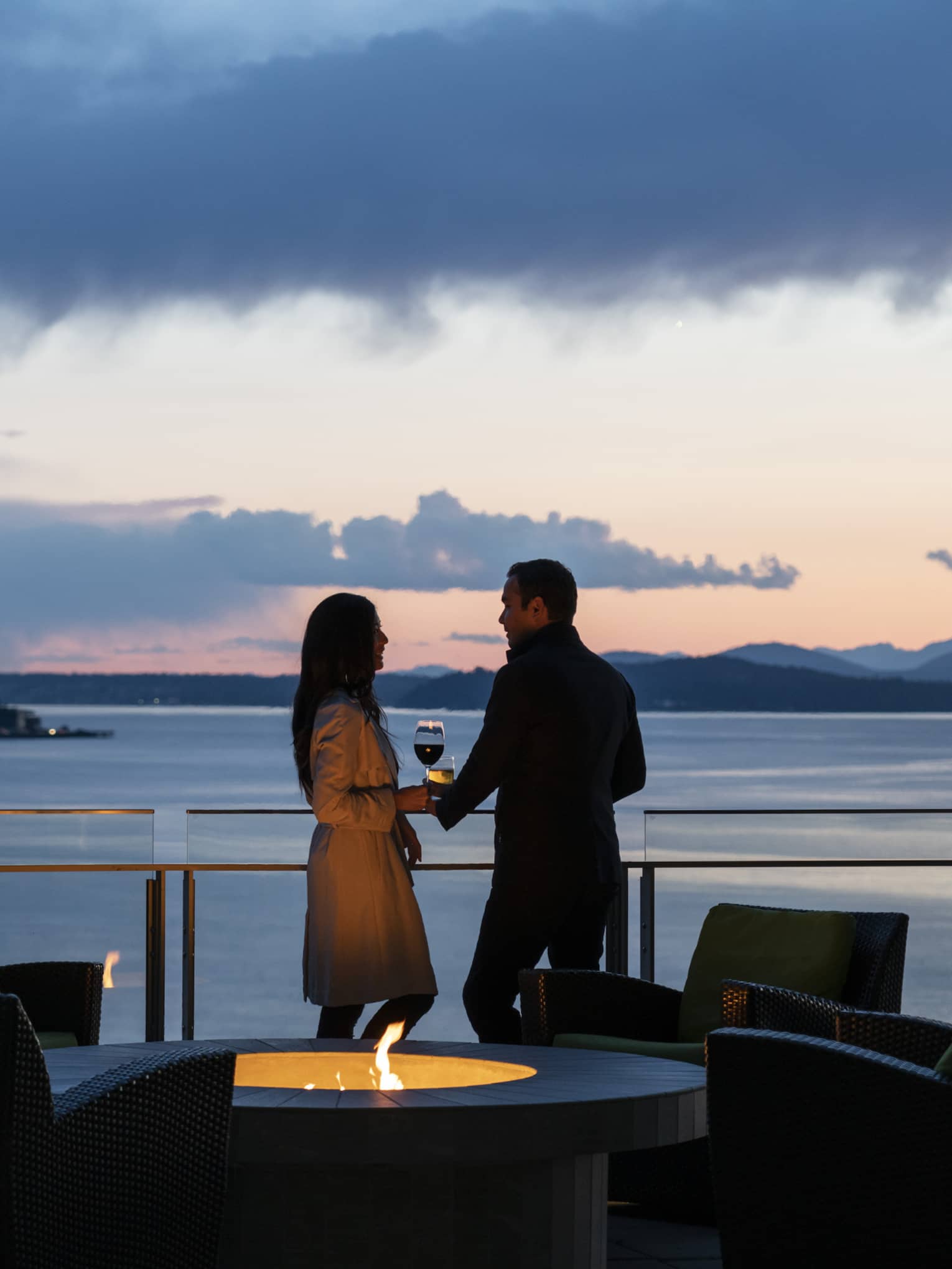 A couple holds hands and shares wine on the balcony as the sun sets