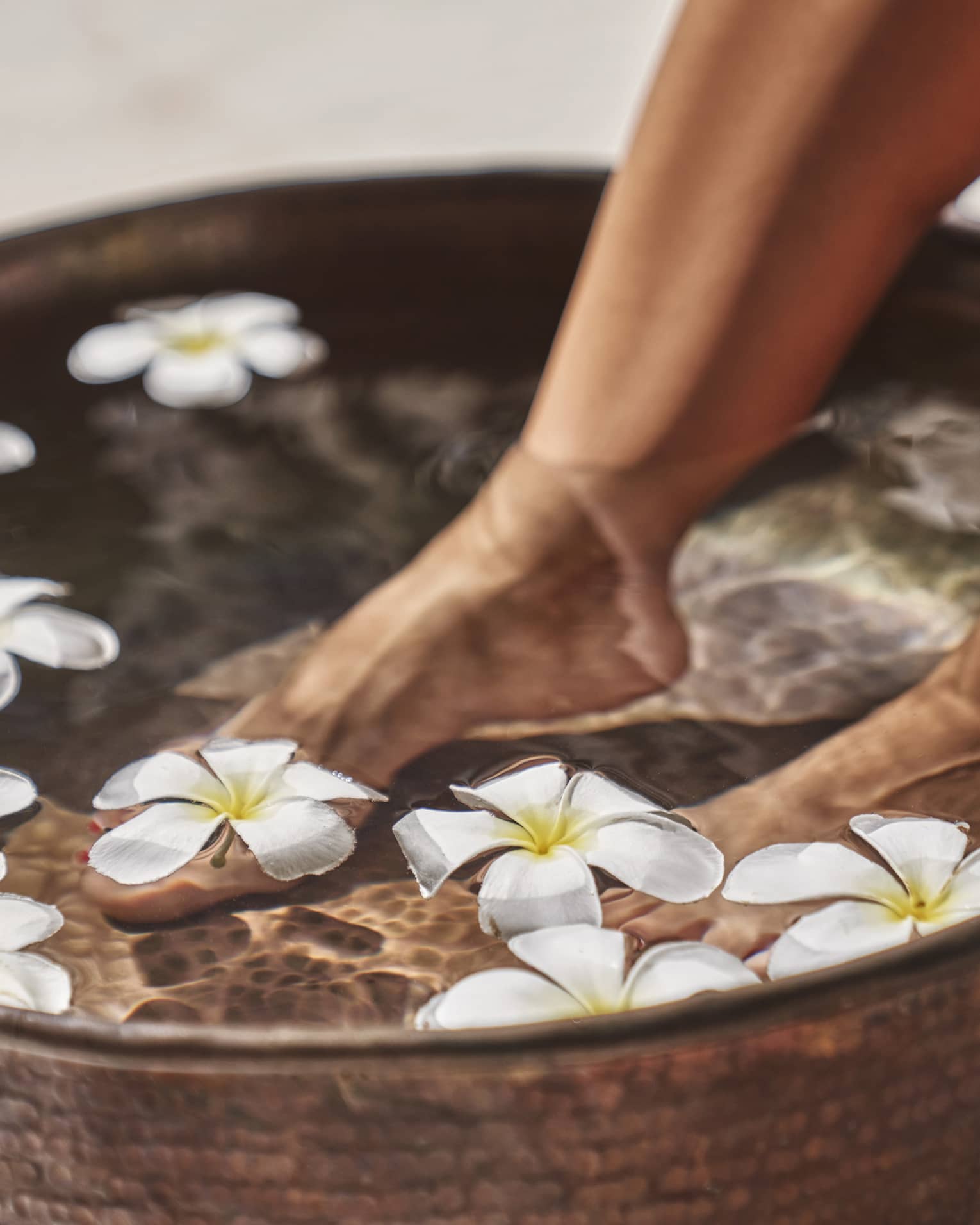 A woman's feet in a bowl of water and flowers.