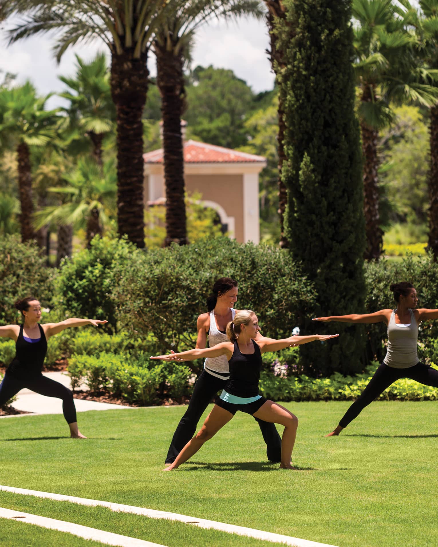 Group of people stand, arms outstretched in yoga poses on green lawn