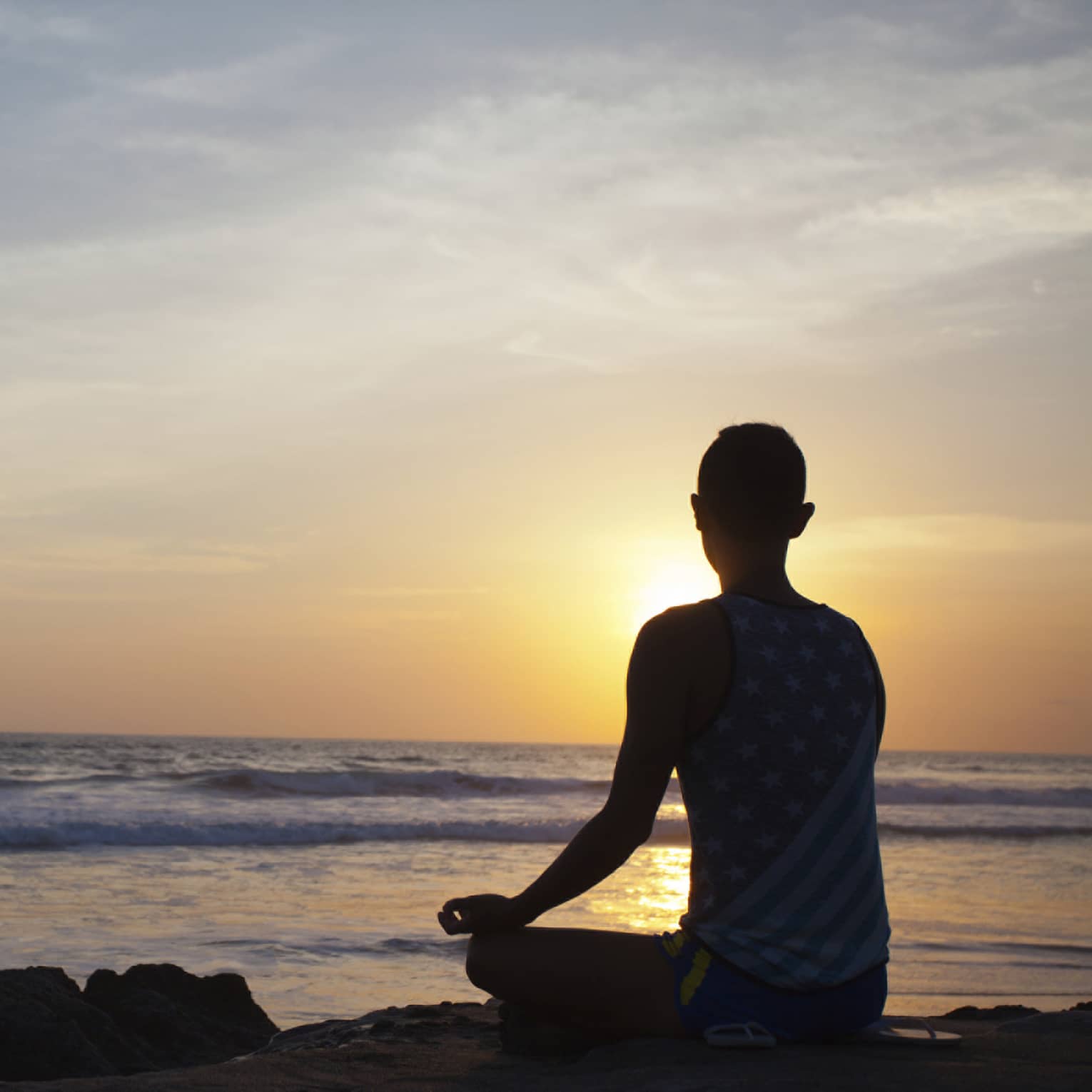 Silhouette of person sitting cross-legged, meditating in front of beach at sunset