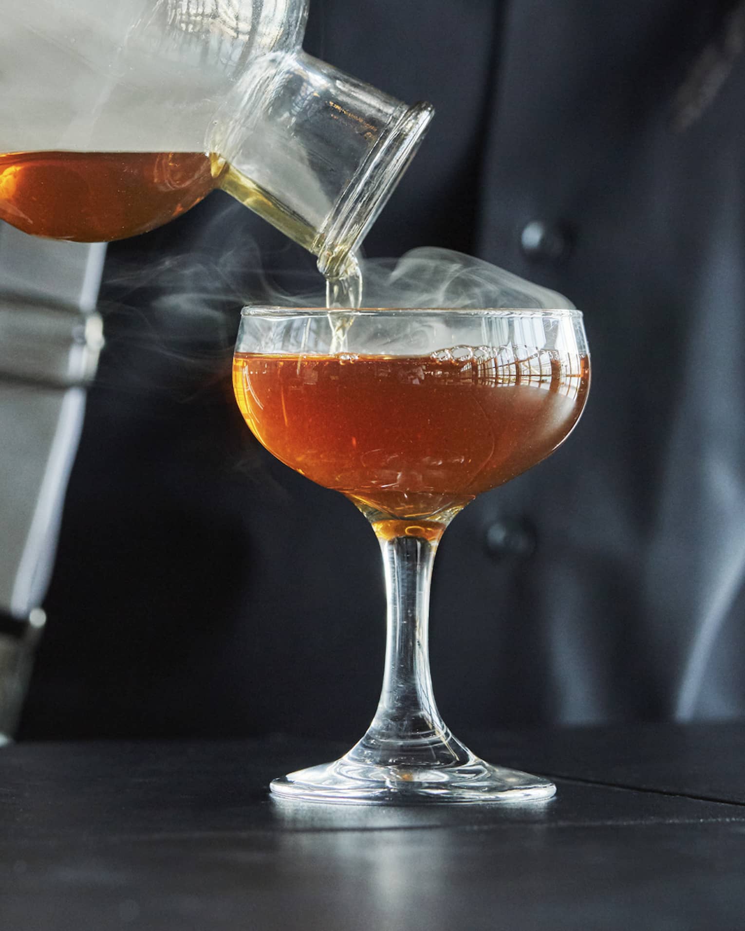 Smoke rolls off the decanter as a Four Seasons staff member pours bourbon into a coupe glass