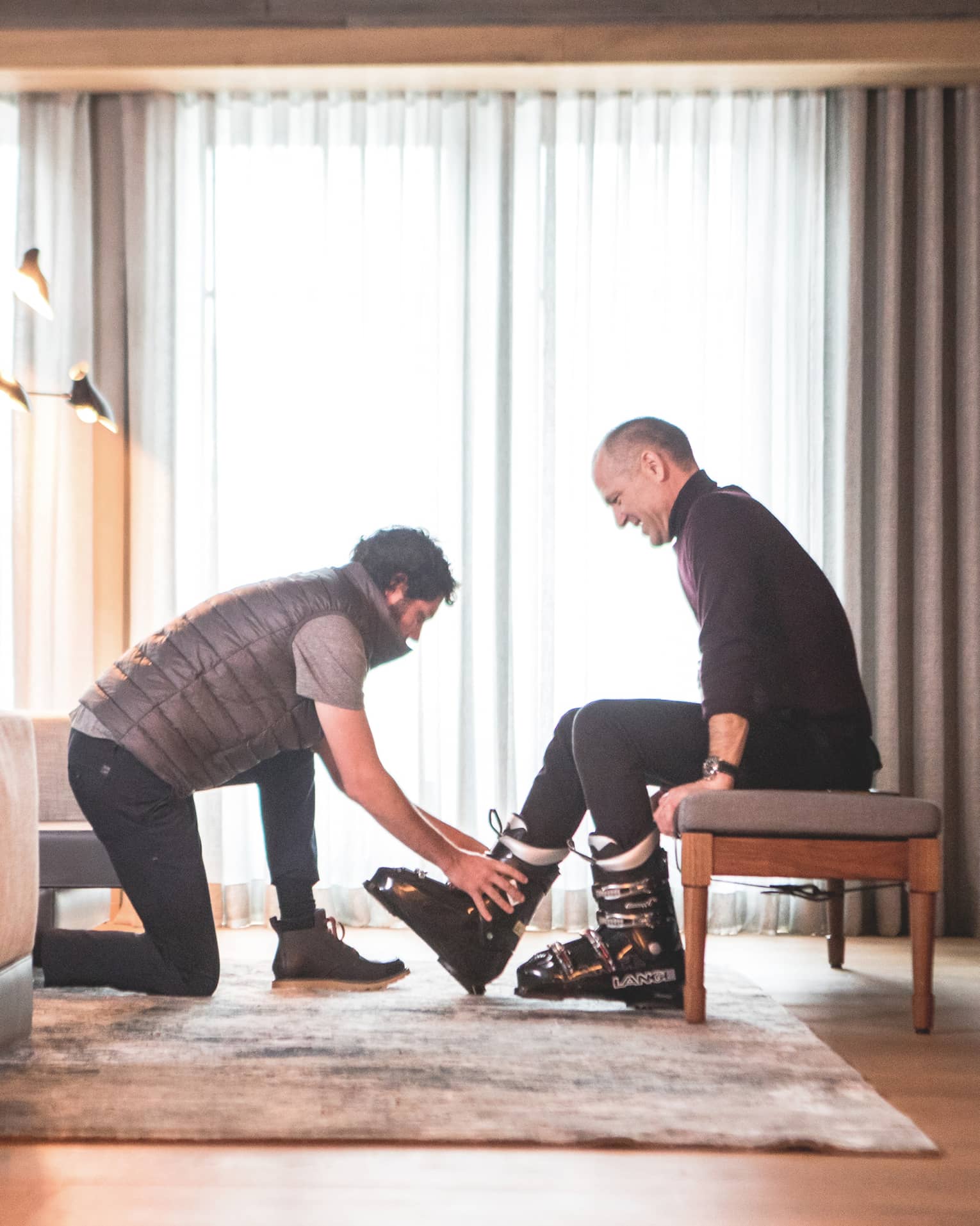 One man helping another to put on ski shoes.