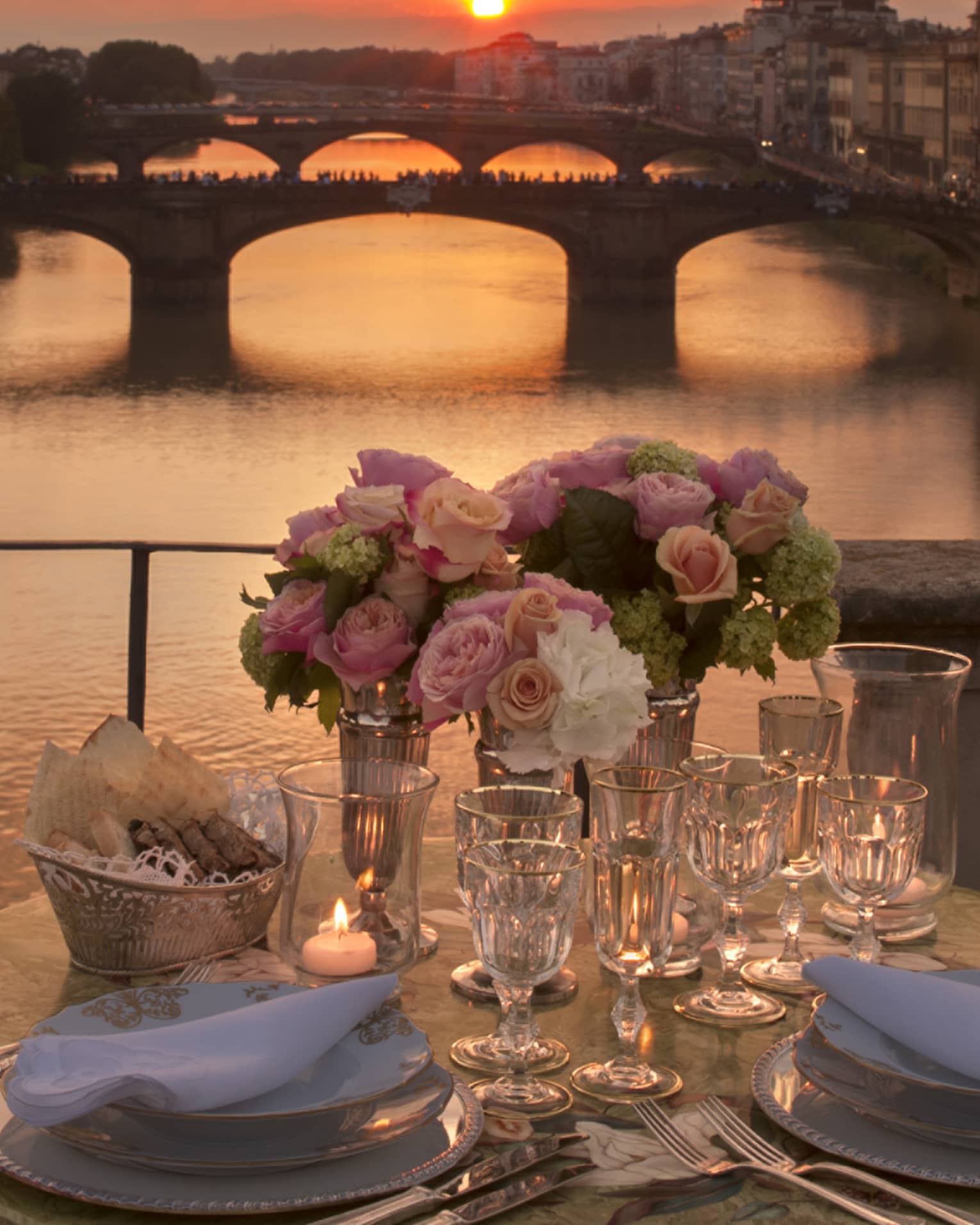 Pink roses in vases on formal dining table on bridge overlooking canal, sunset