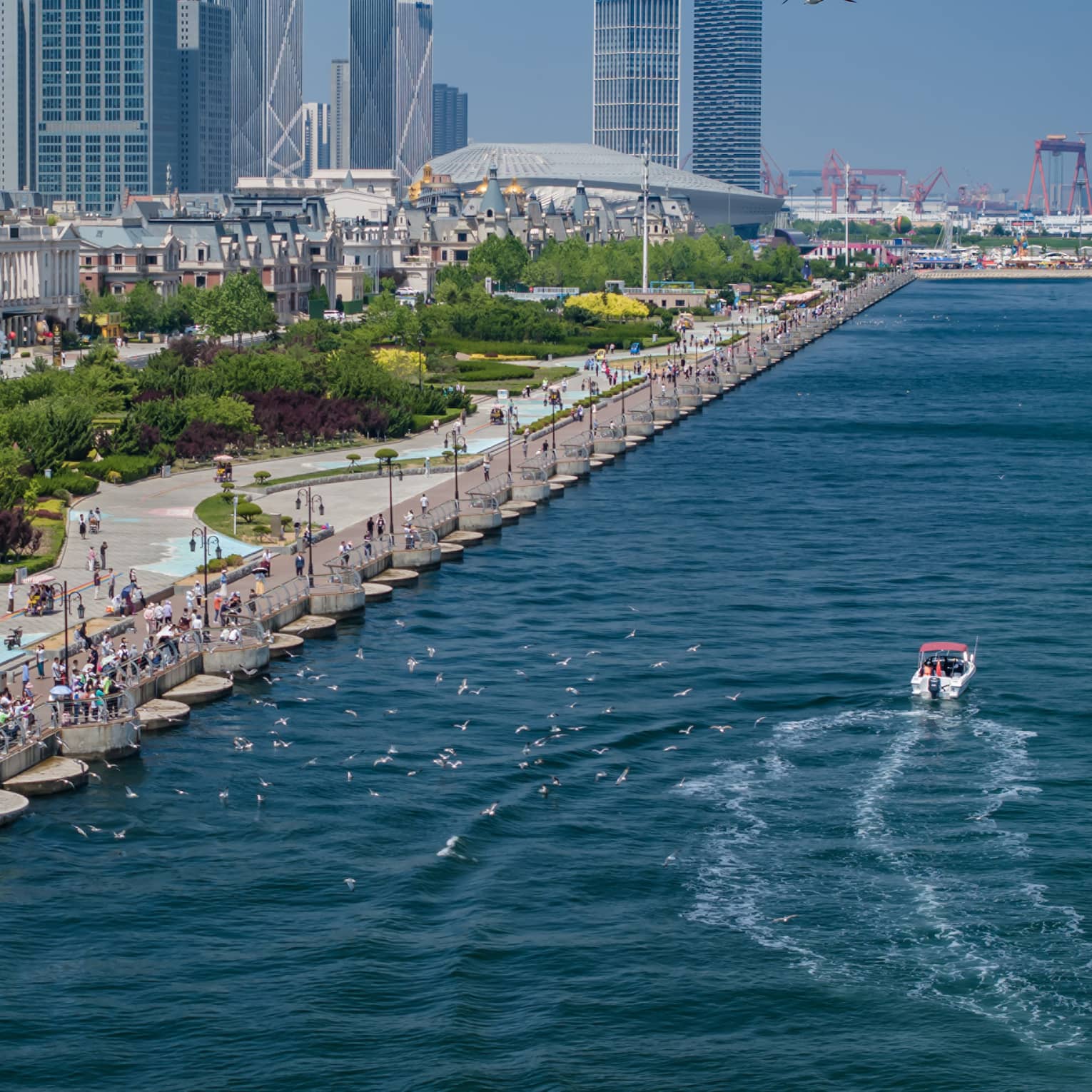 Aerial view of water along the pier of a bustling boulevard bordered by lush parkland, old buildings and modern high-rises.