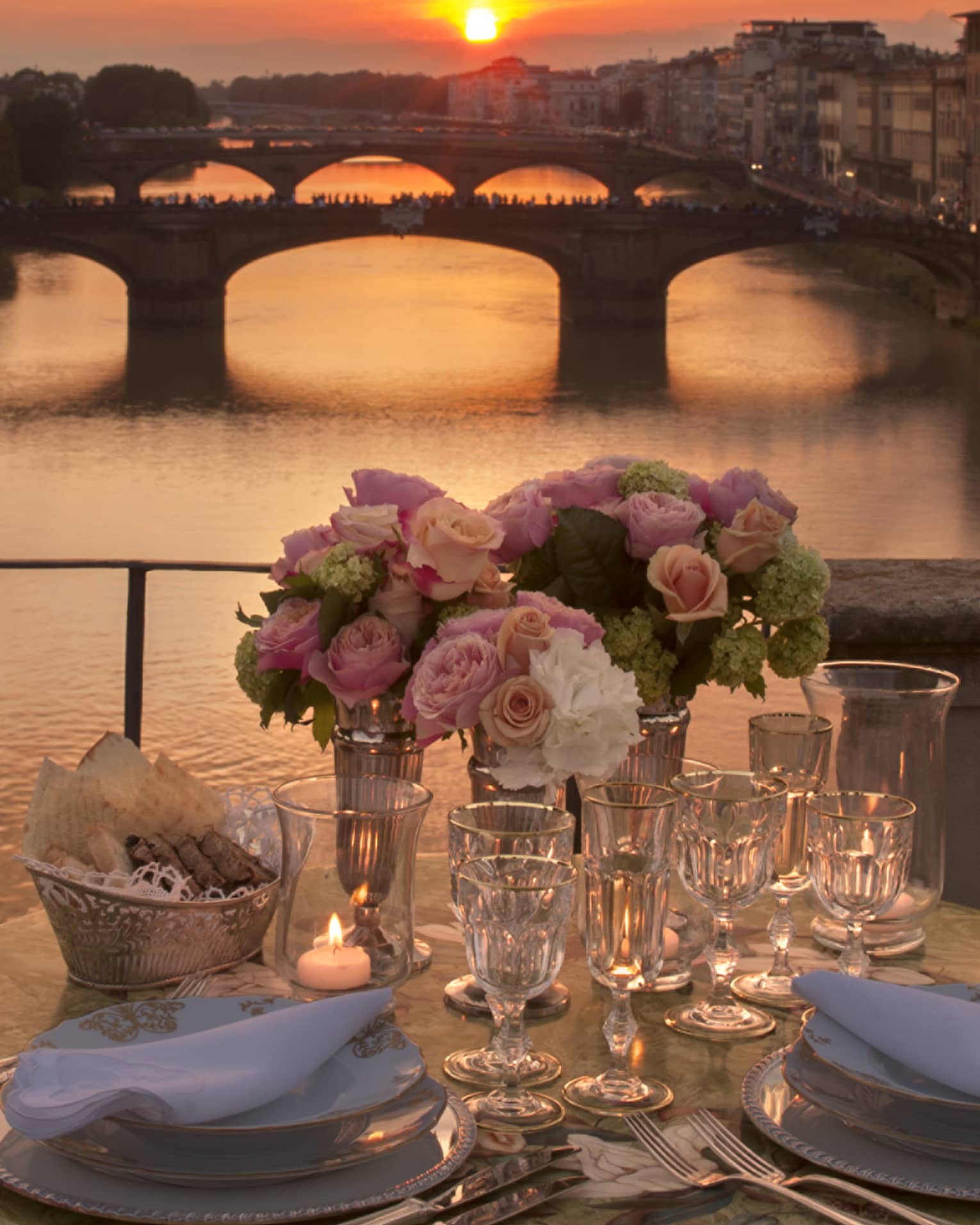 Pink roses in vases on formal dining table on bridge overlooking canal, sunset