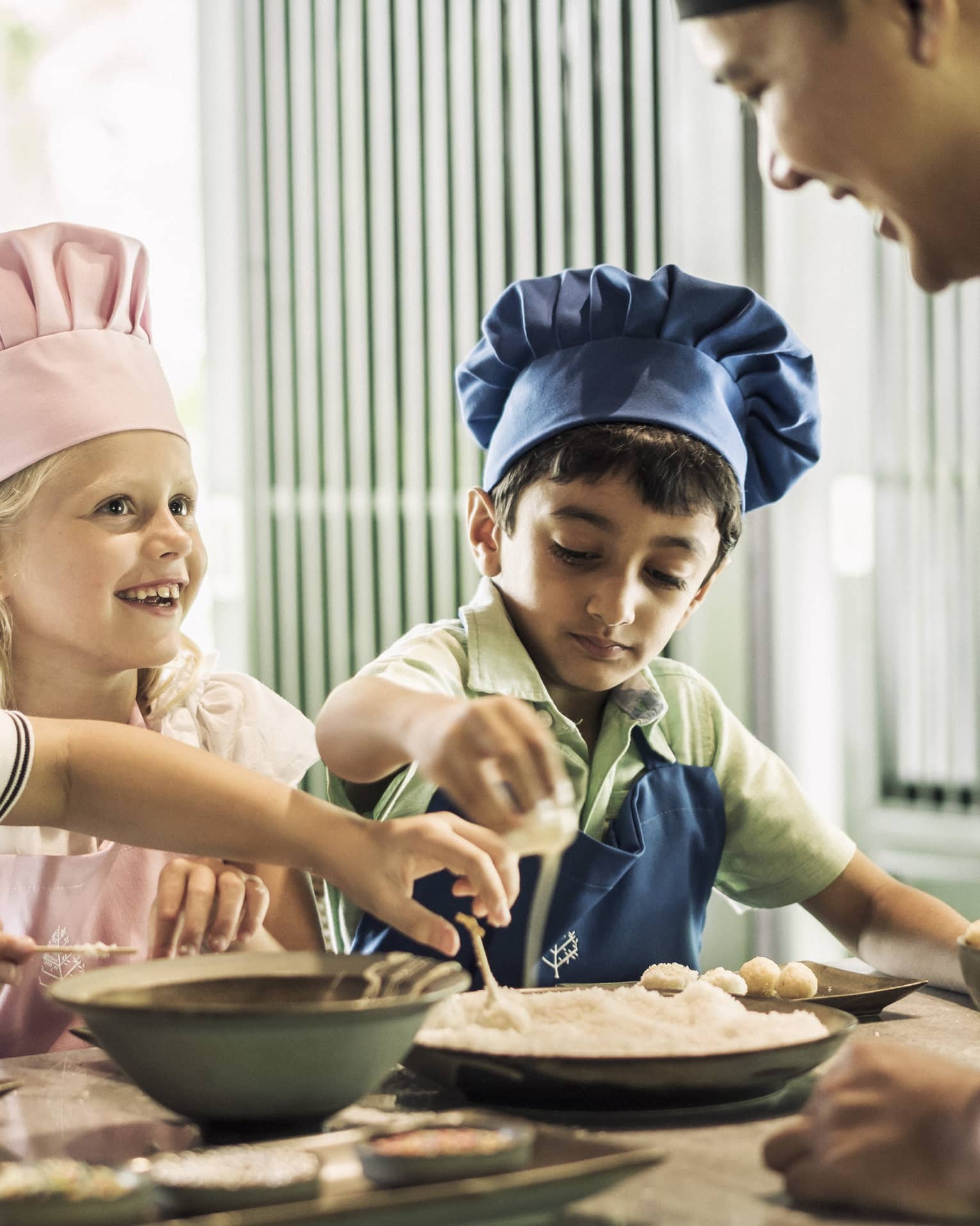 Three children with pink or blue chefs hats making food.
