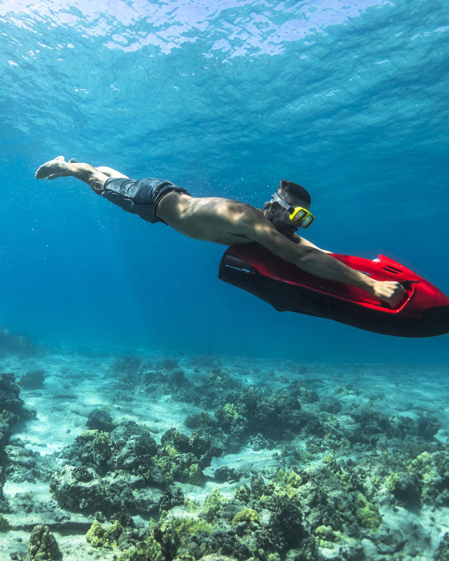 Man dives in ocean over coral, holding red inflatable board