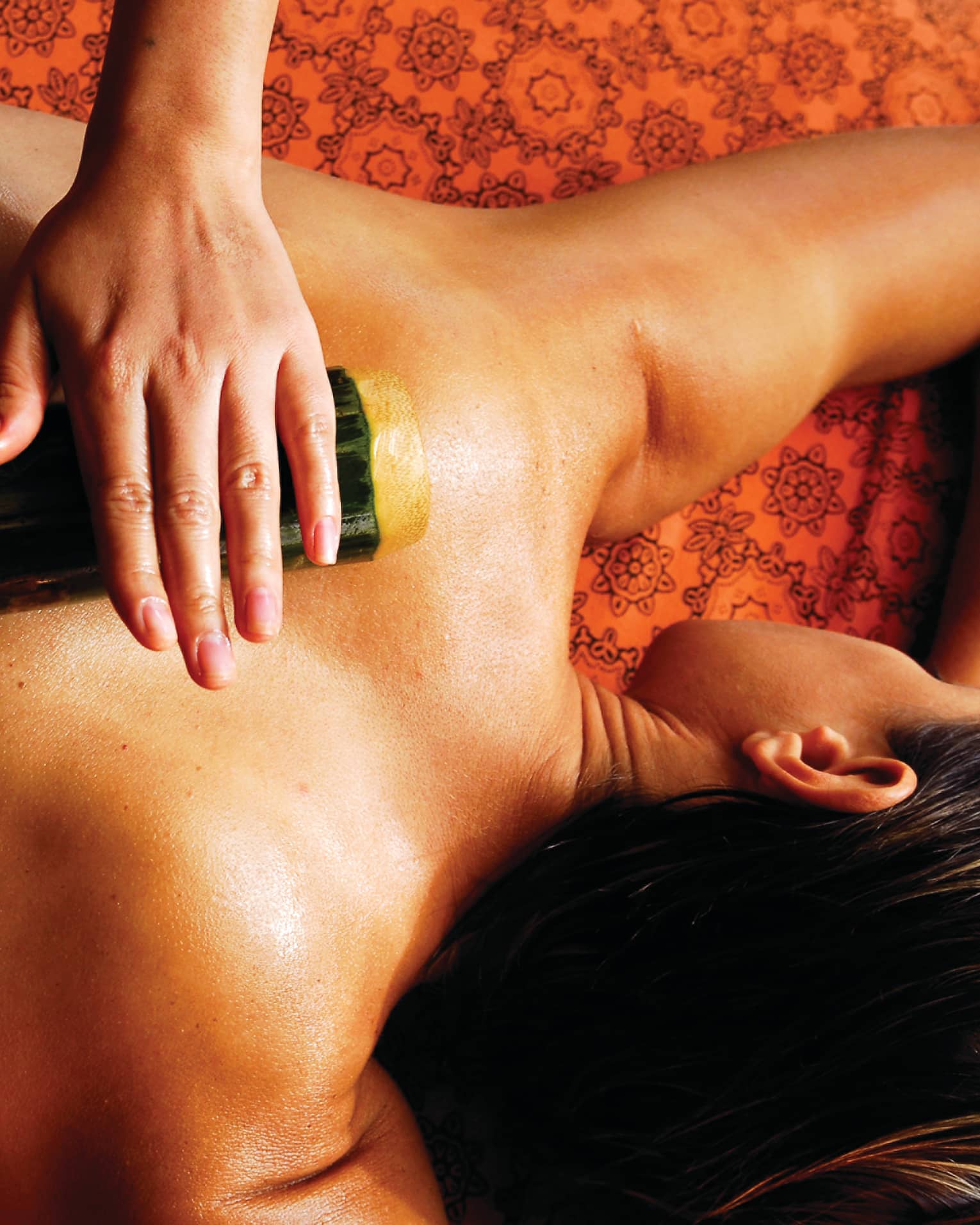 Spa staff rolls thick bamboo stick over woman's bare back, shoulders 