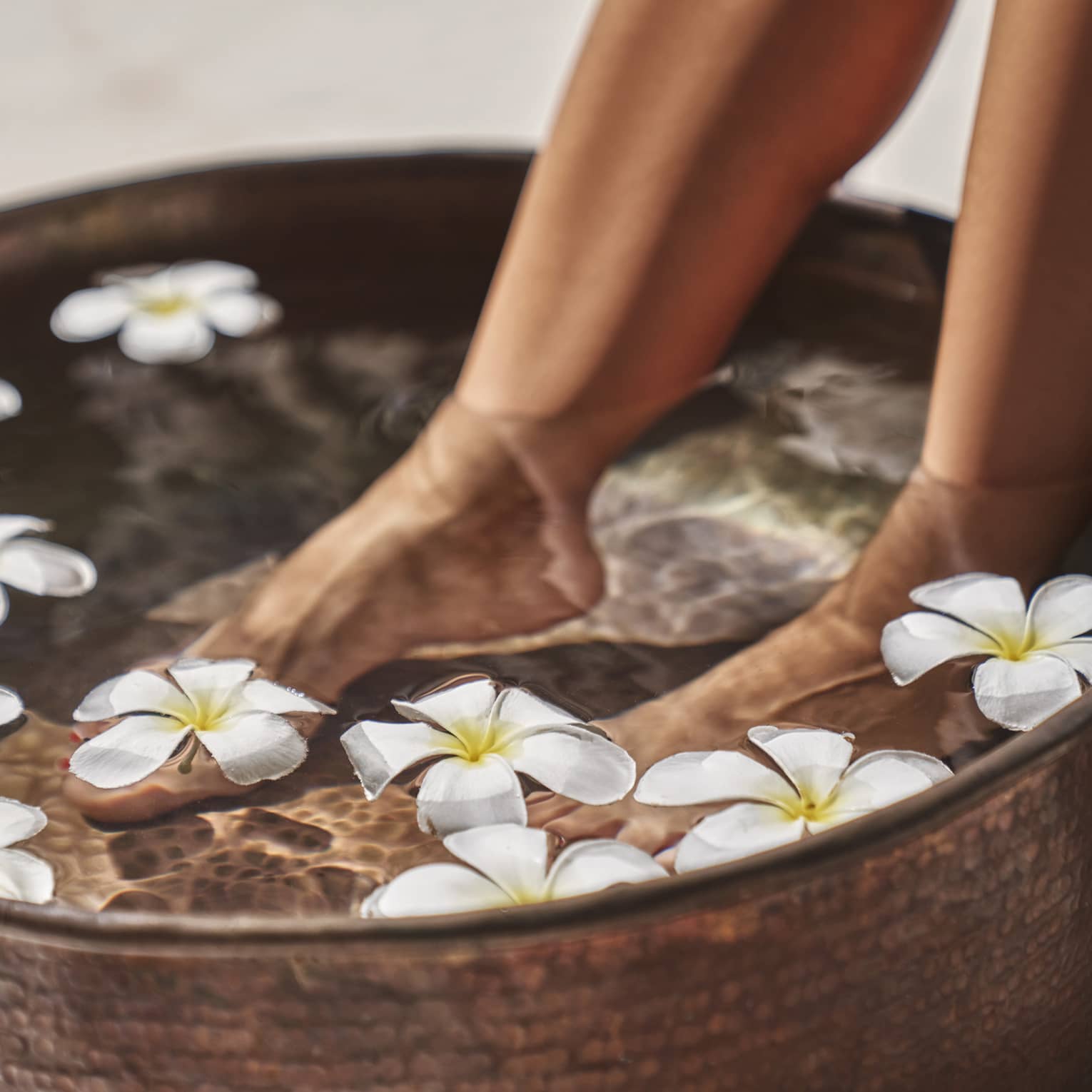 A woman's feet in a bowl of water and flowers.