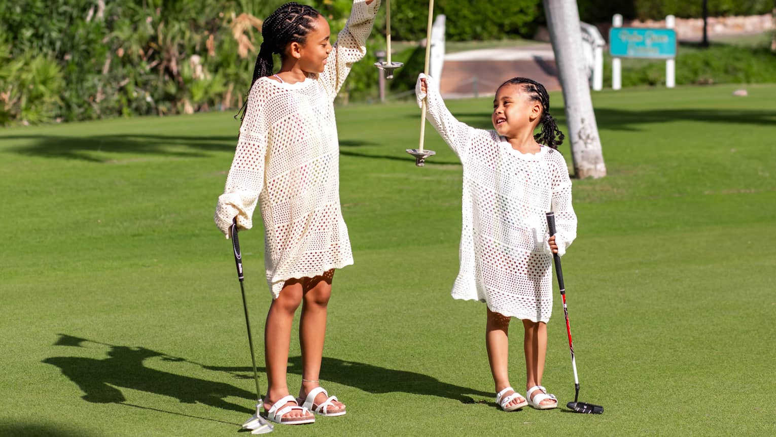 Two kids holding golf clubs and standing on a  golf course on a sunny day