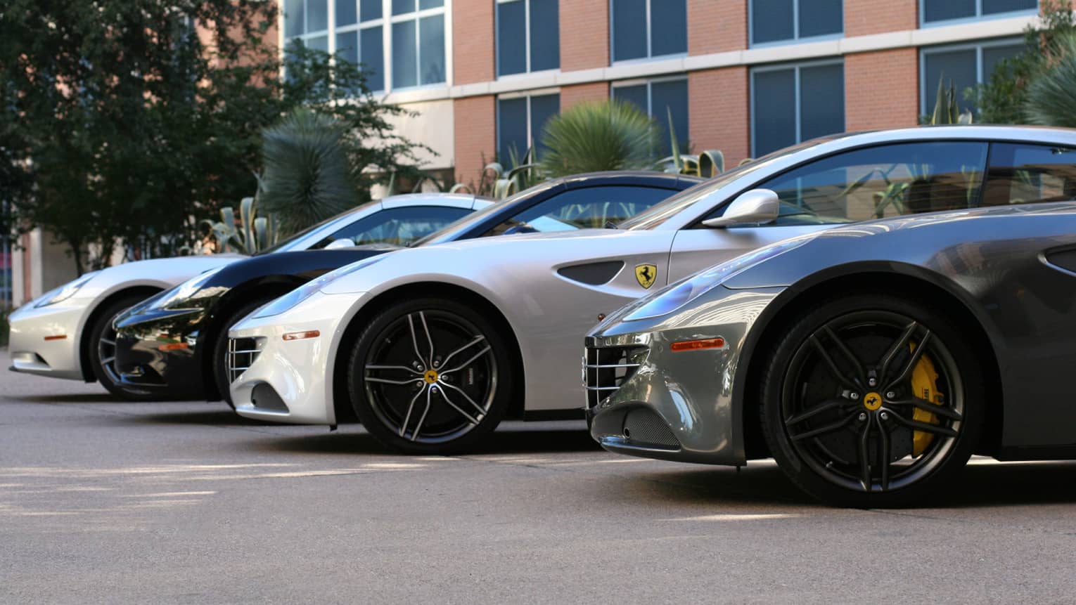 Front side view of luxury Ferrari cars parked in a row in sunny parking lot