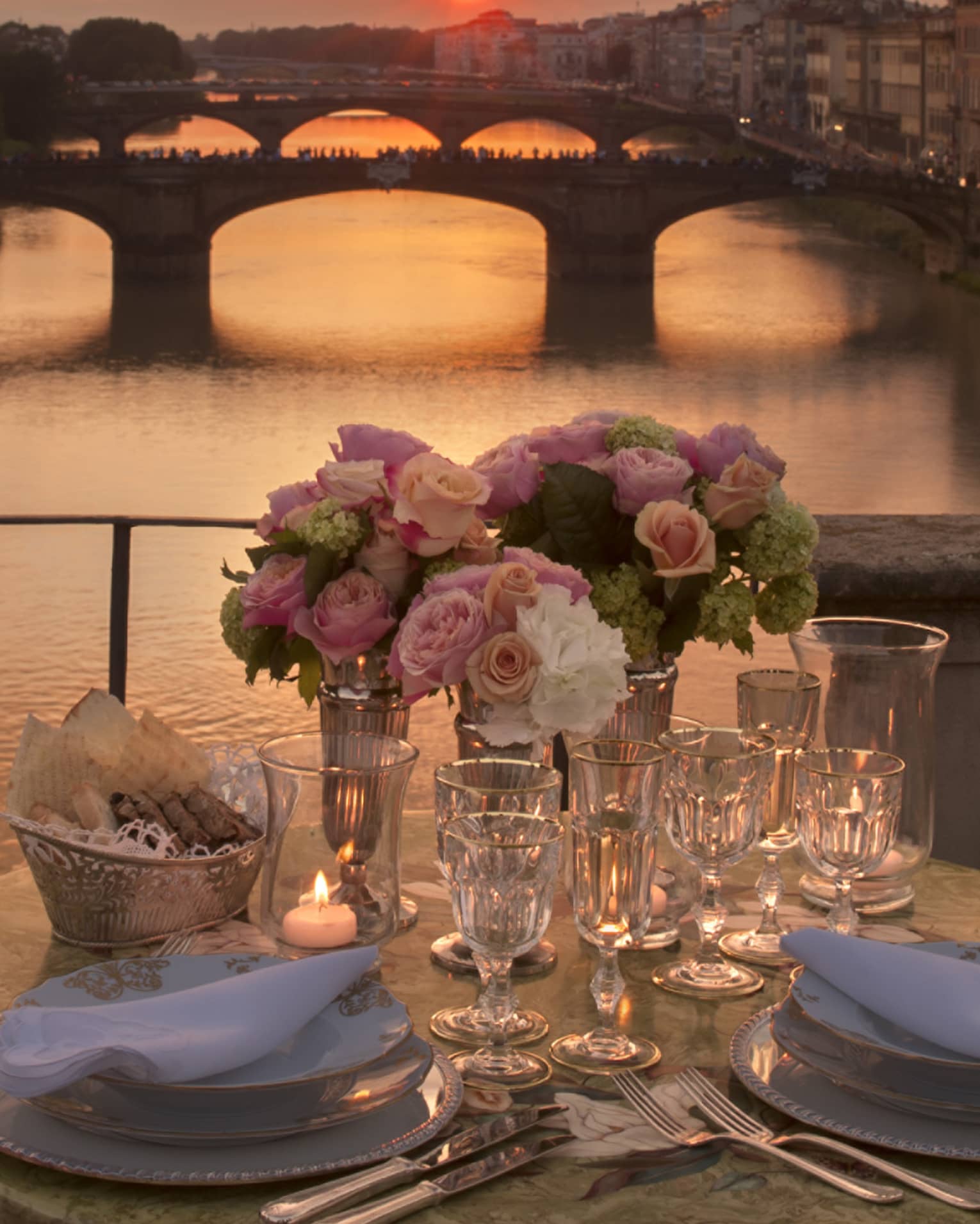 Pink roses in vases on formal dining table on bridge overlooking canal, sunset