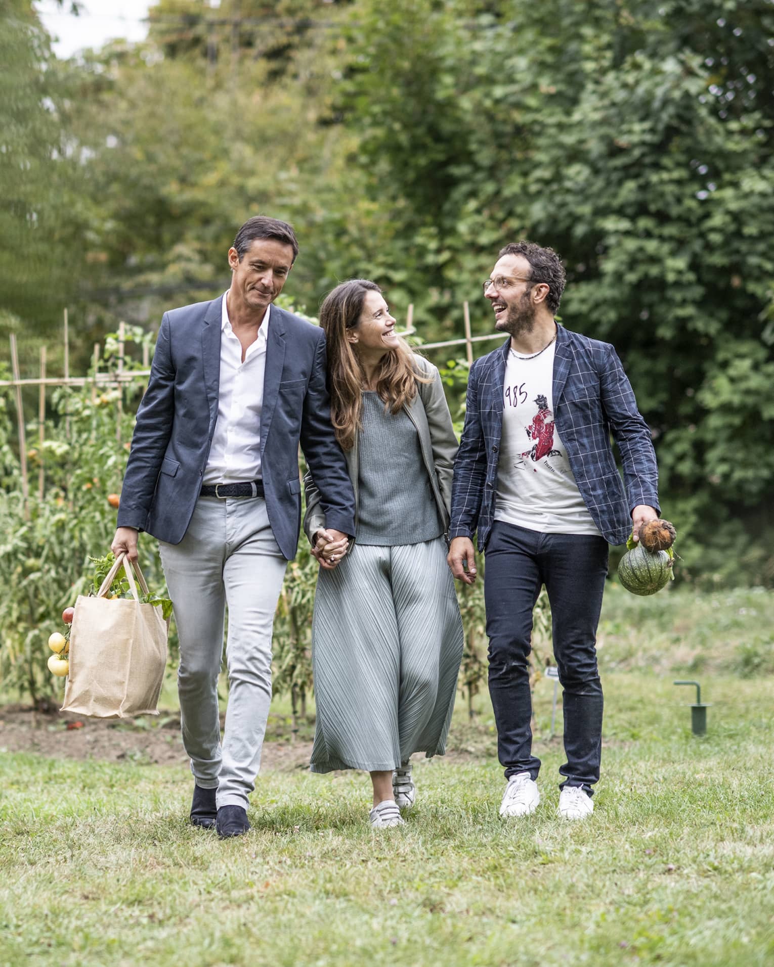 Three people holding bags with fresh produce walk away from vegetable garden