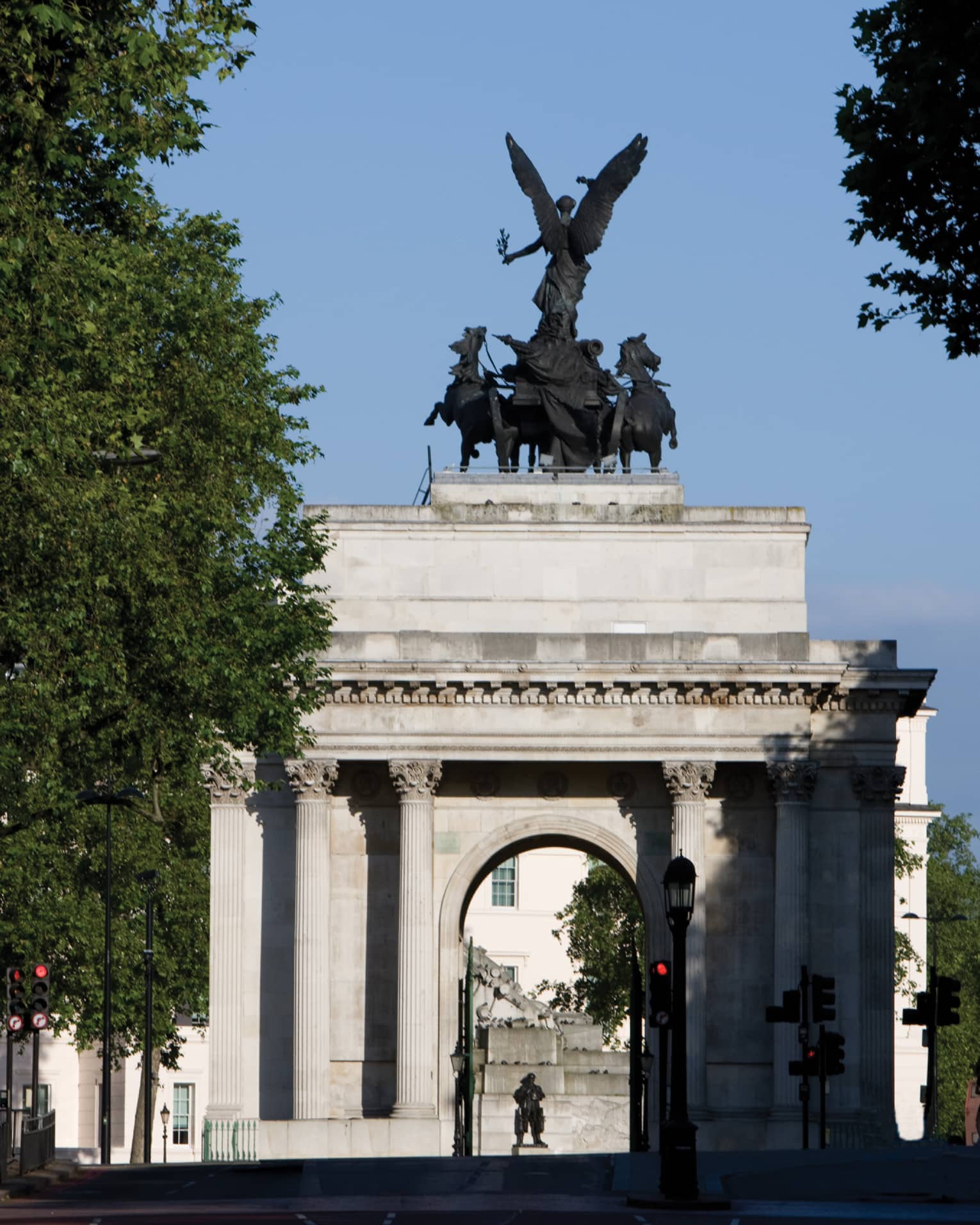 View through trees to Wellington Arch monument and statue against blue sky