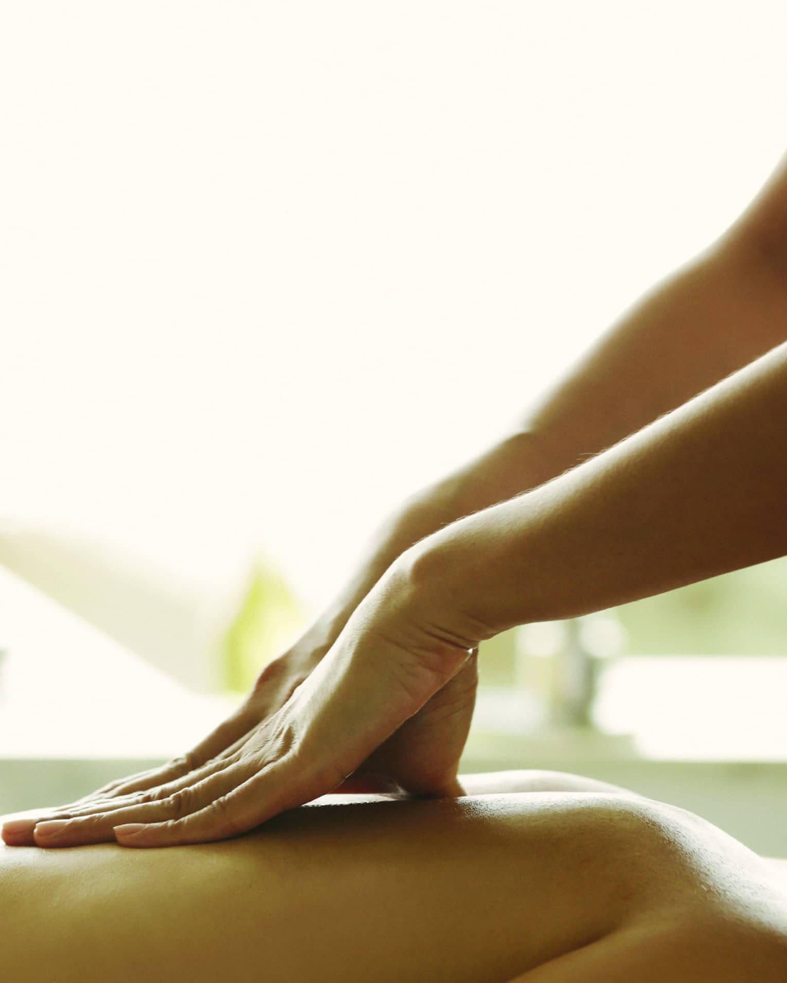 Masseuse reaches over, massages woman's bare back as she lies on spa table