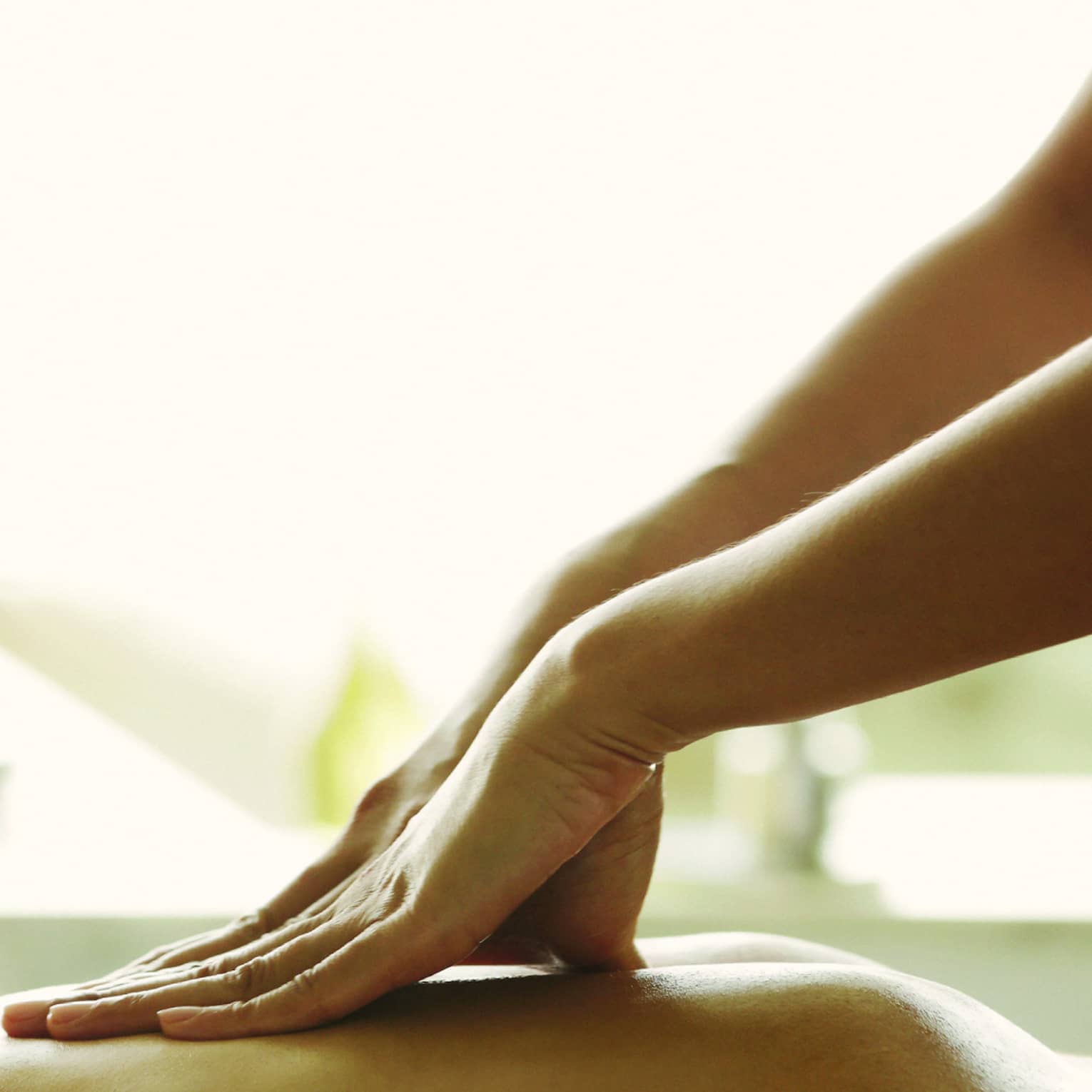 Masseuse reaches over, massages woman's bare back as she lies on spa table