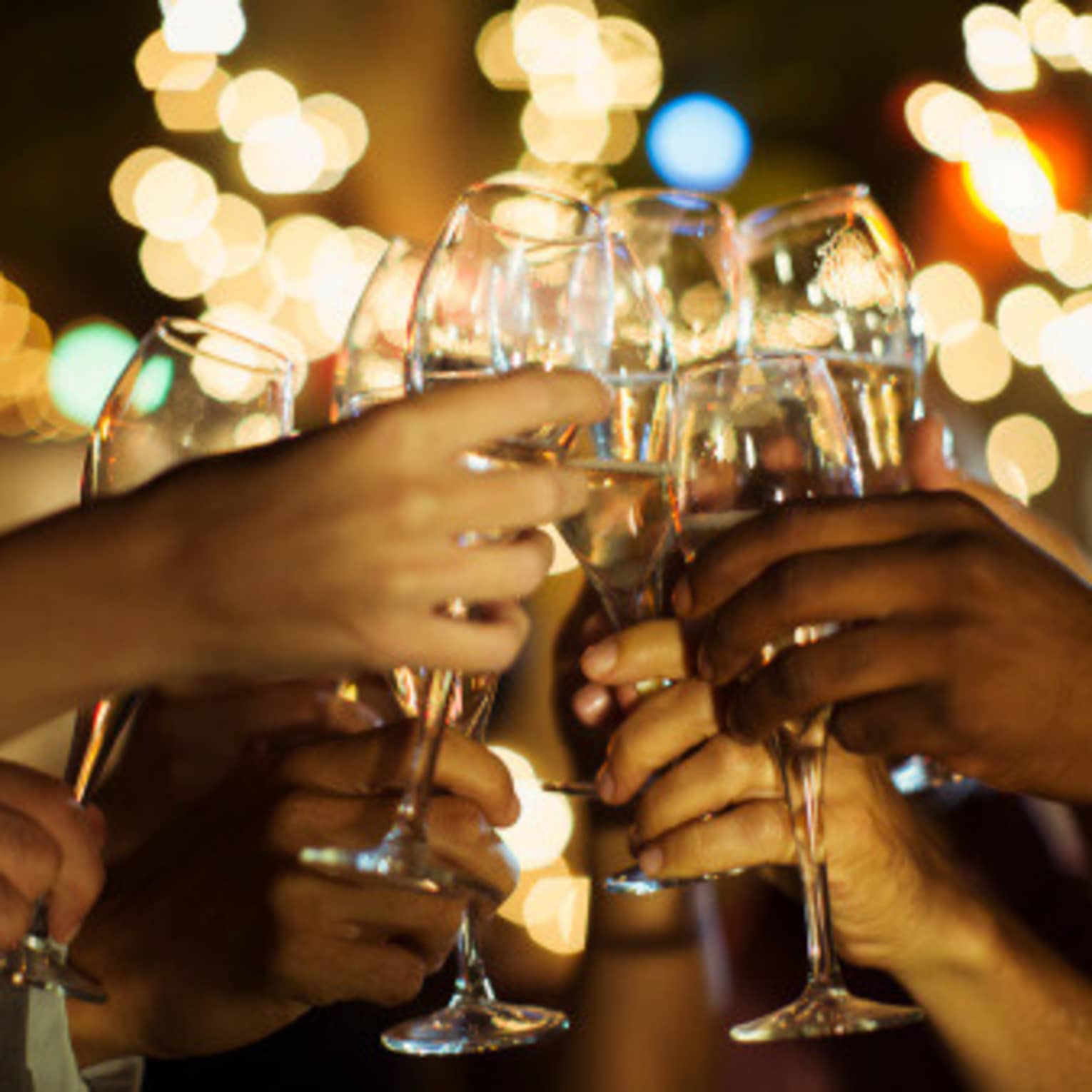 A group of guests clink their glasses of champagne together on a patio with twinkle lights