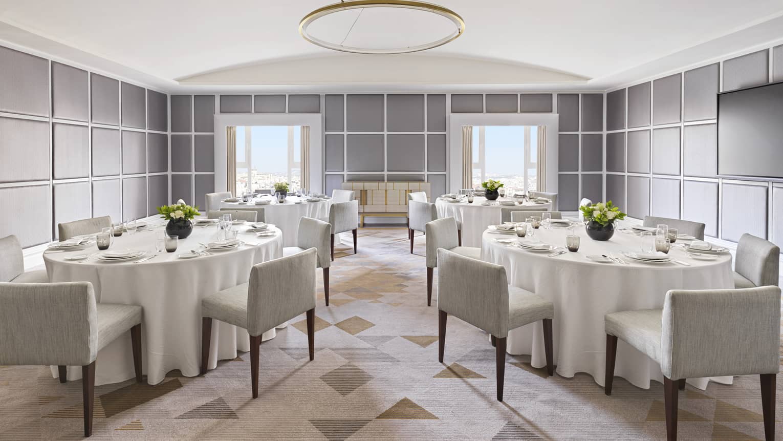 Several tables with white linens and square grey chairs.