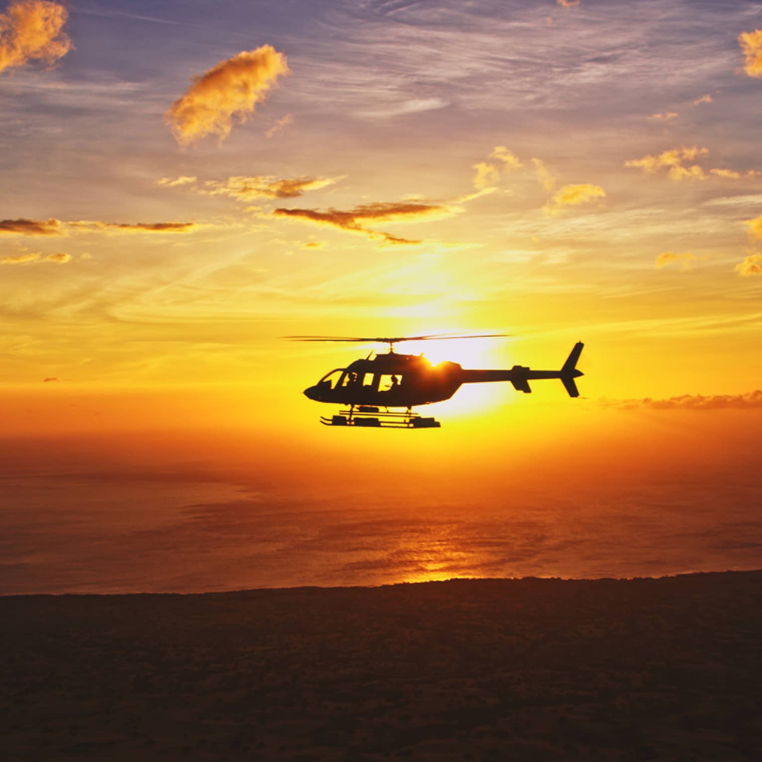 Silhouette of helicopter against orange sunset
