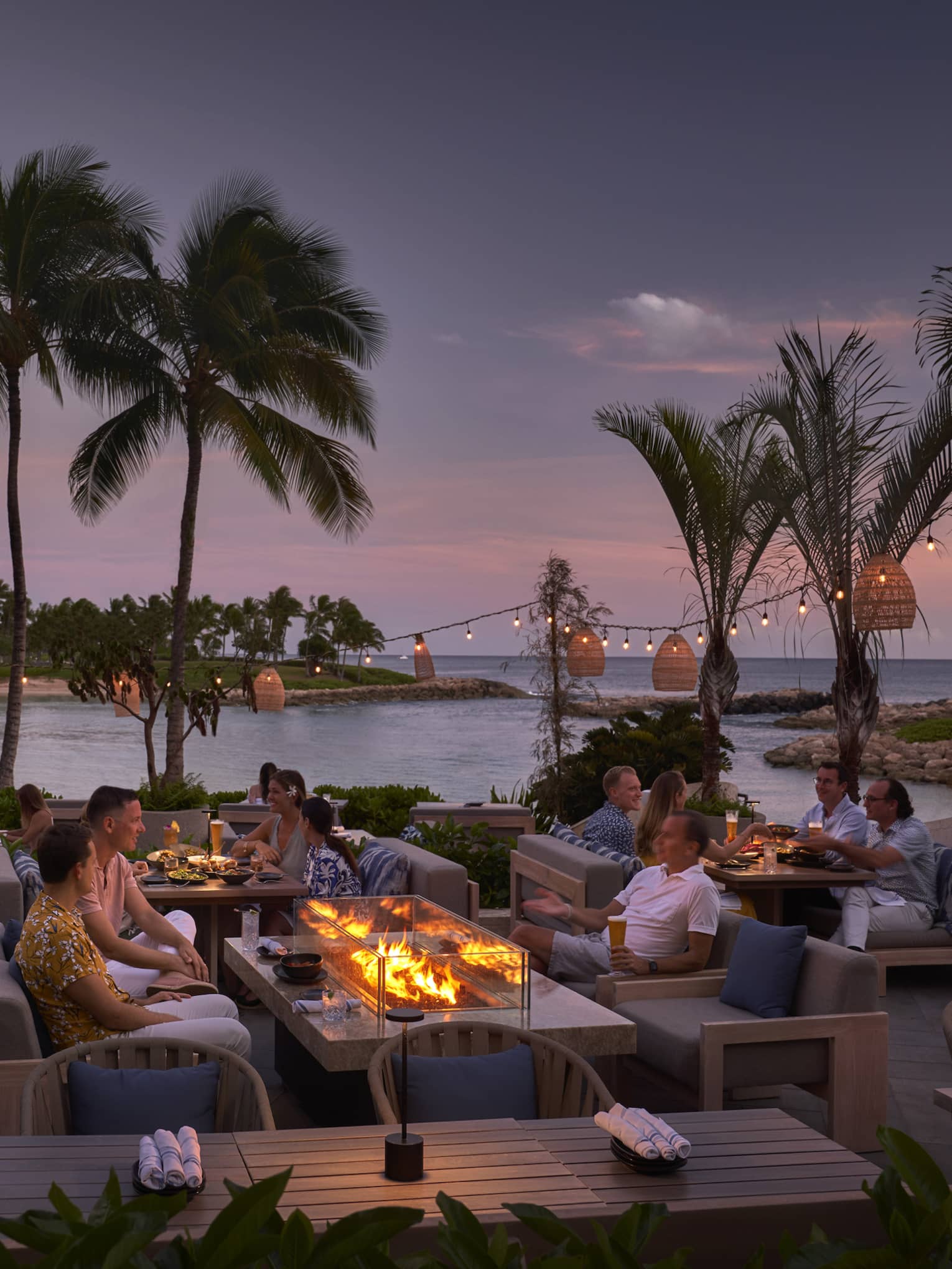 People mingling on outdoor, waterfront terrace in tropical location at night