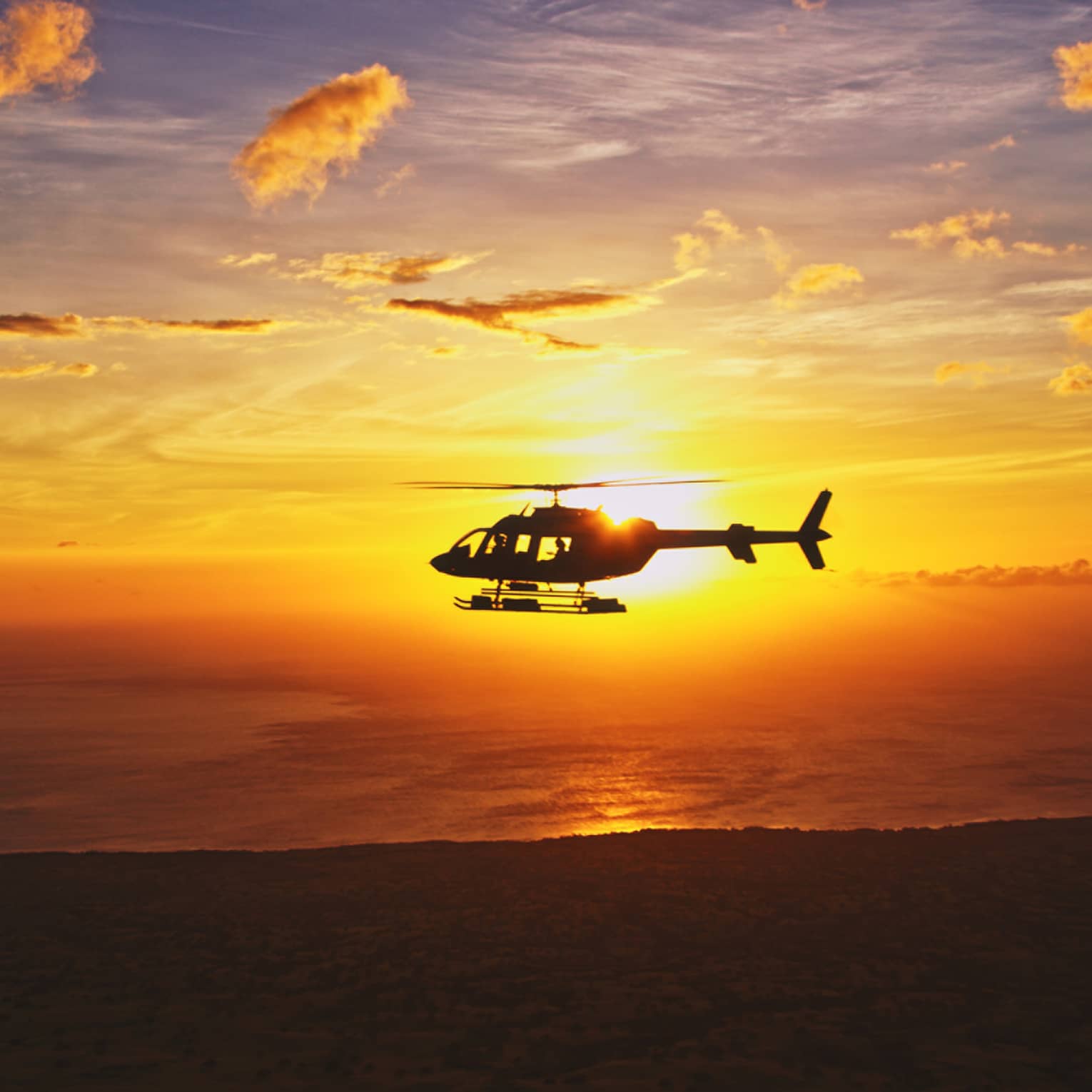 Silhouette of helicopter against orange sunset