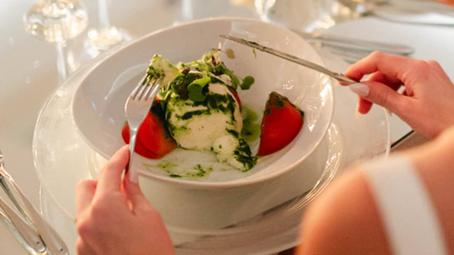 Person in bridal gown sits at round table set for dinner, fork and knife posed to dig into a meal
