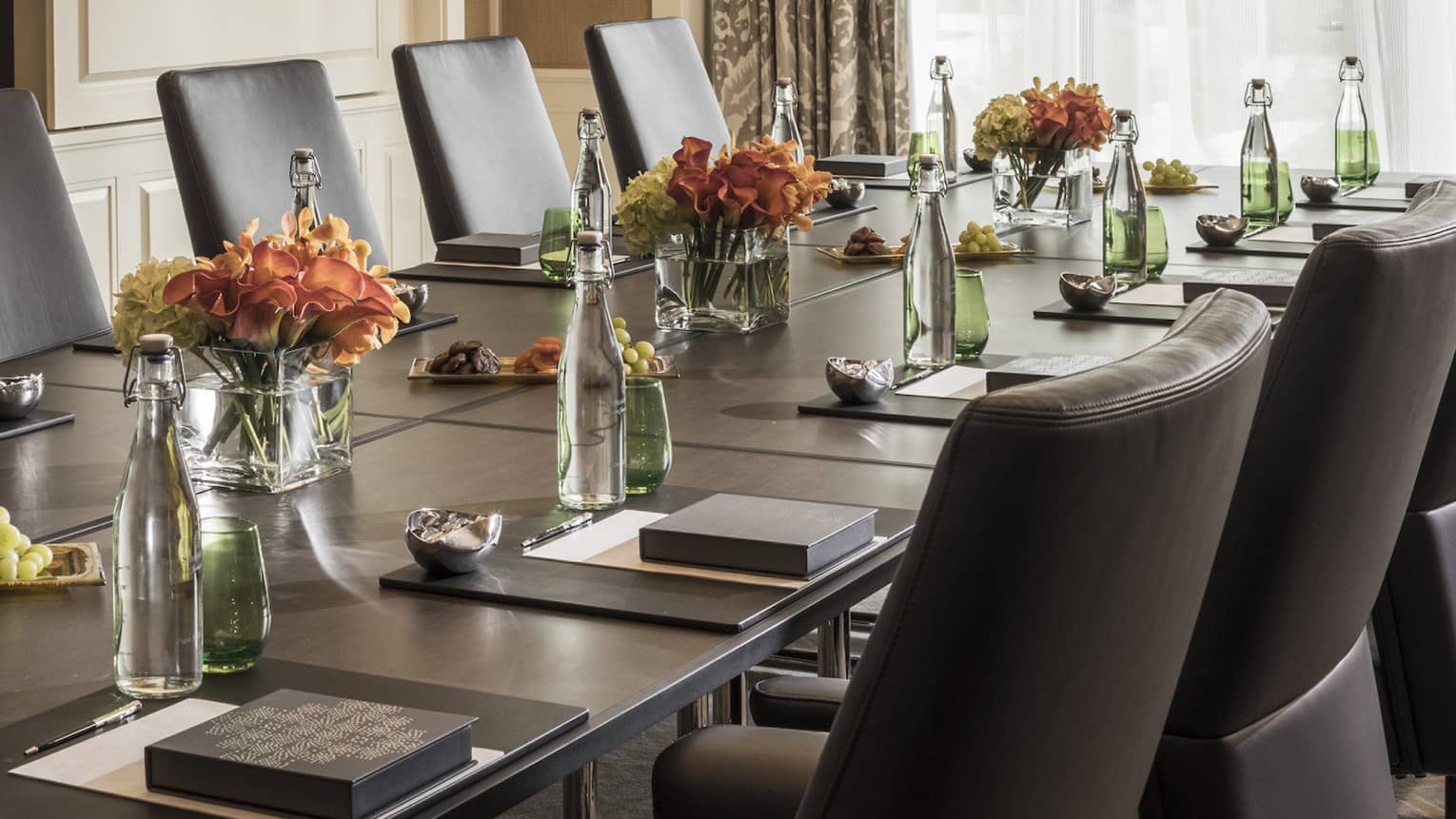 Long boardroom table set with glass bottles of water, flowers in bright meeting room