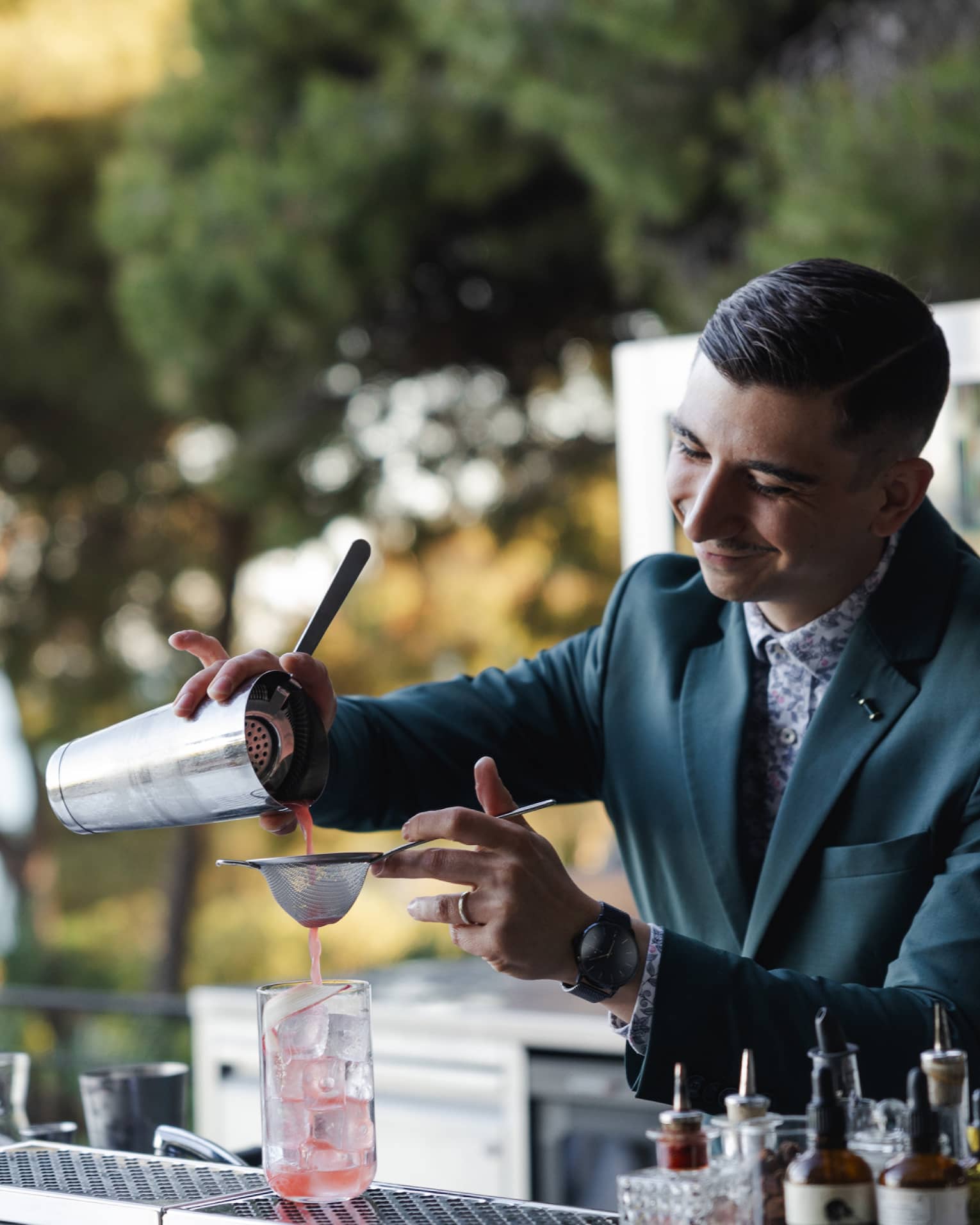 A bartender pours a pink beverage through a strainer into a glass with ice