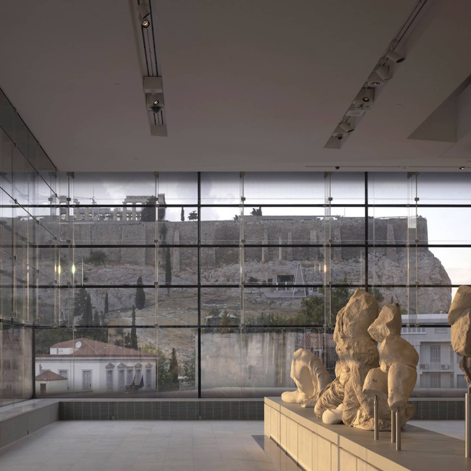 Greek sculptures on display in glass room overlooking ruins at Acropolis Museum