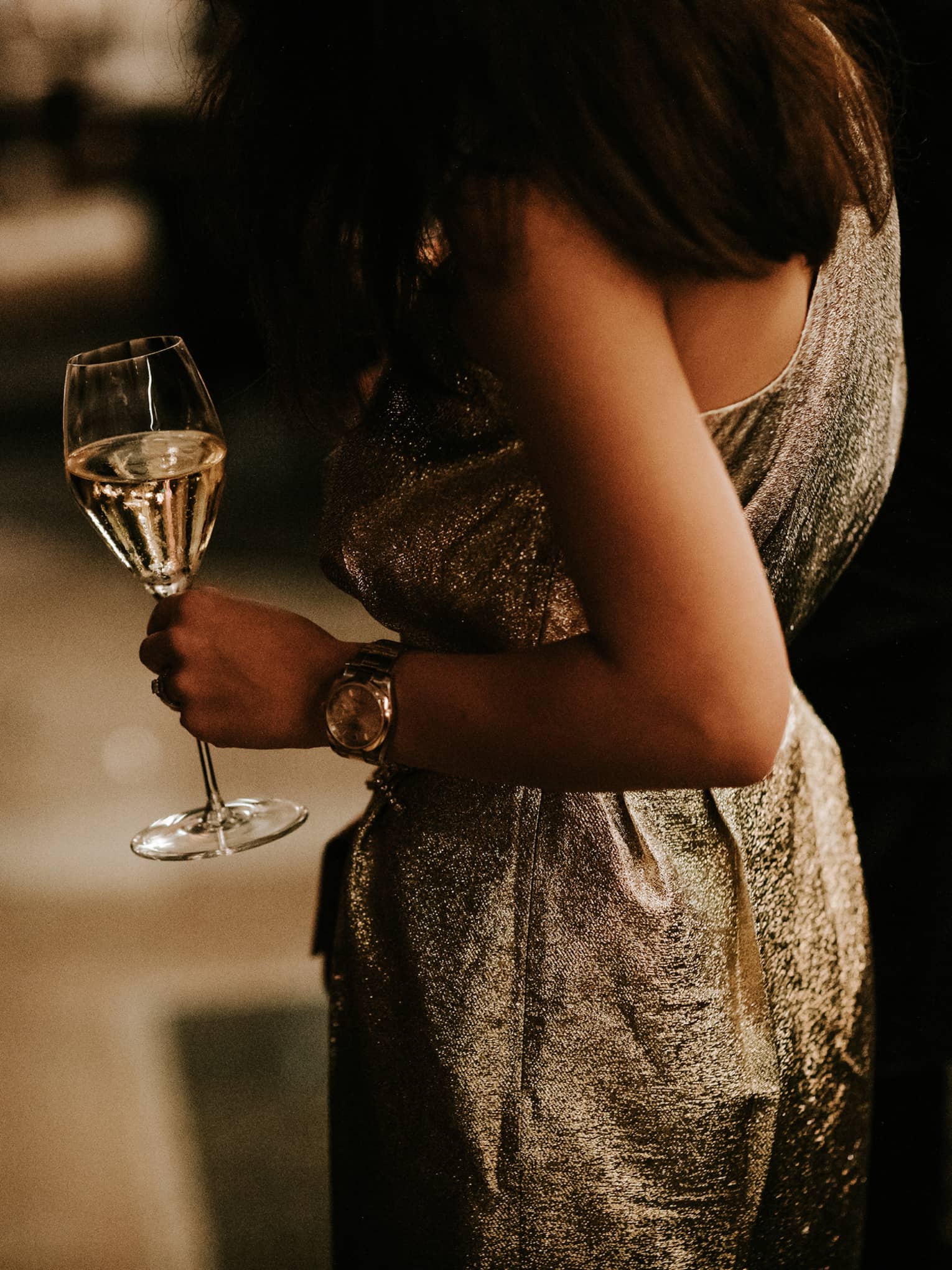 Woman in gold dress holding a glass of white wine