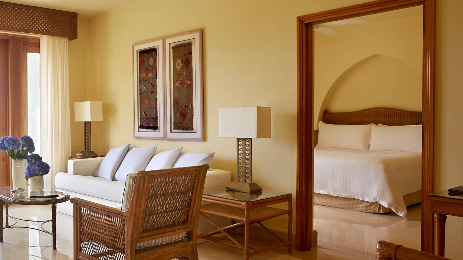 Poolside family suite living room with sofa, wicker chair, table with fresh flowers in front of sunny balcony door