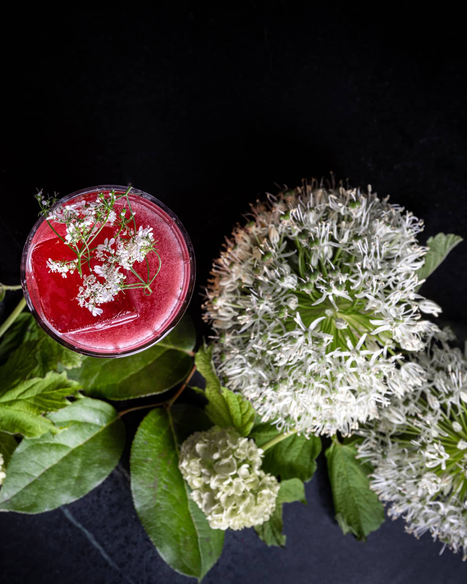 Flowers and a red cocktail on a dark background.