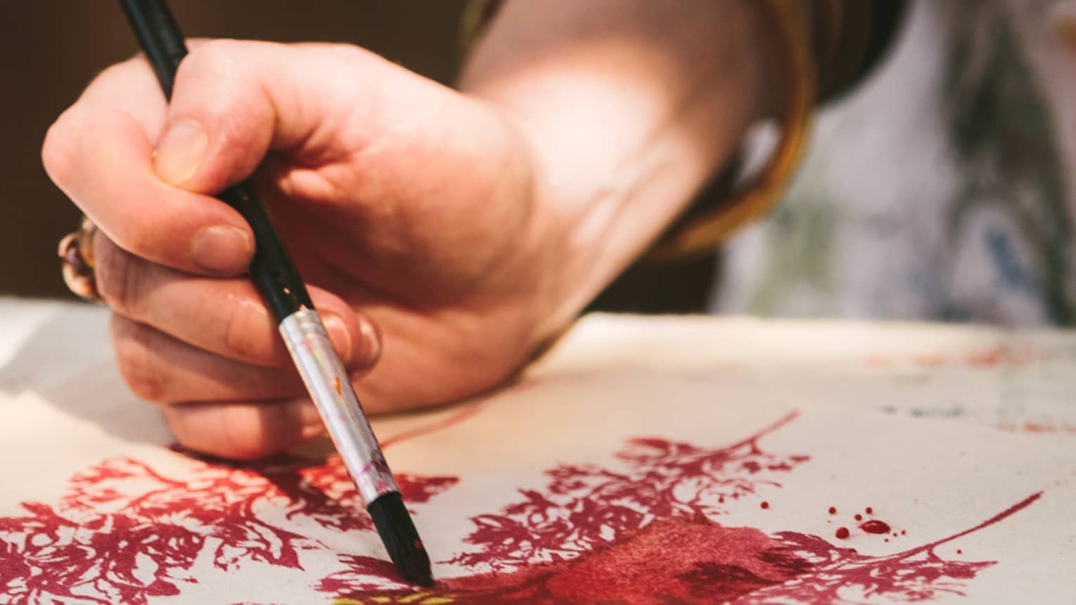 Close-up of woman with paint brushes painting flowers on canvas bag