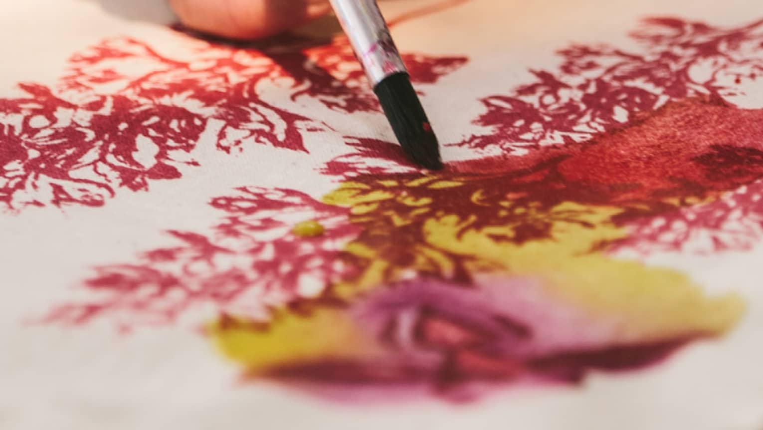 Close-up of woman with paint brushes painting flowers on canvas bag
