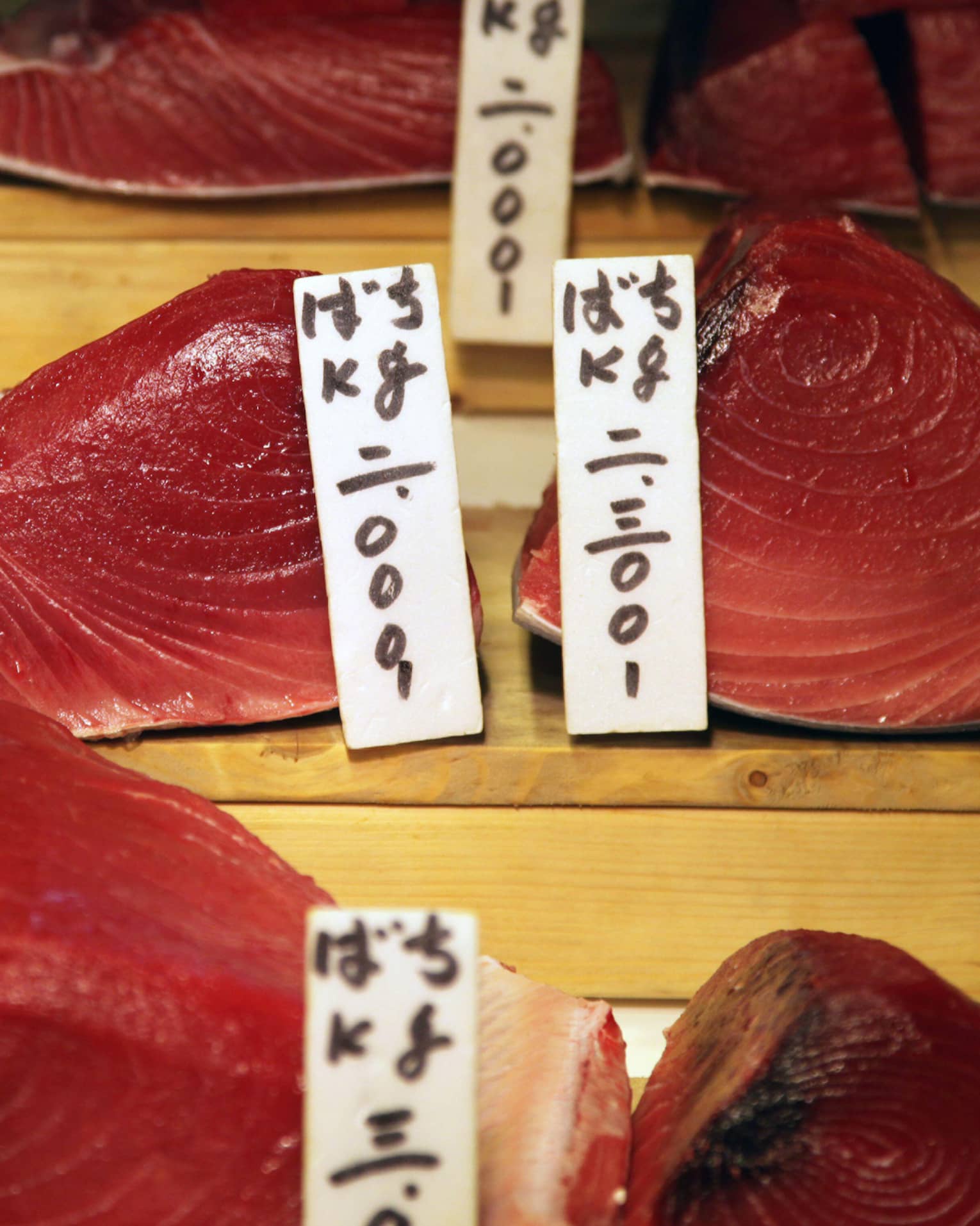 Close-up view of labelled cuts of glistening, pinky-red fresh tuna displayed on three levels of wooden risers.