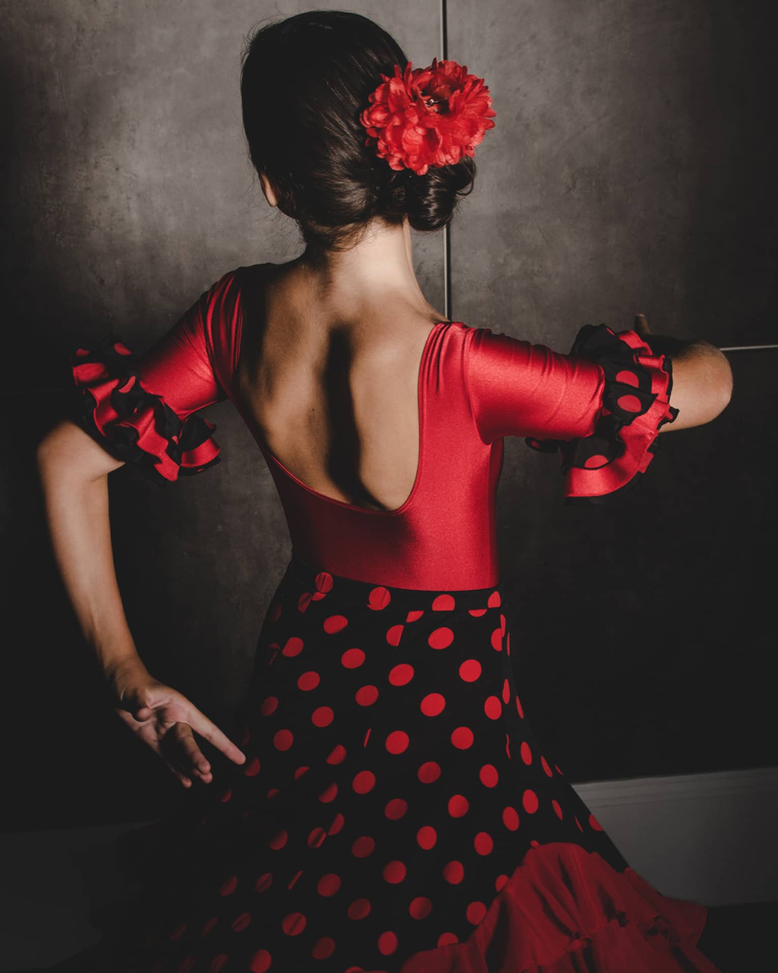 A woman wearing a black and white salsa dancing dress and red flower in her hair dances with her face turned away from the camera 