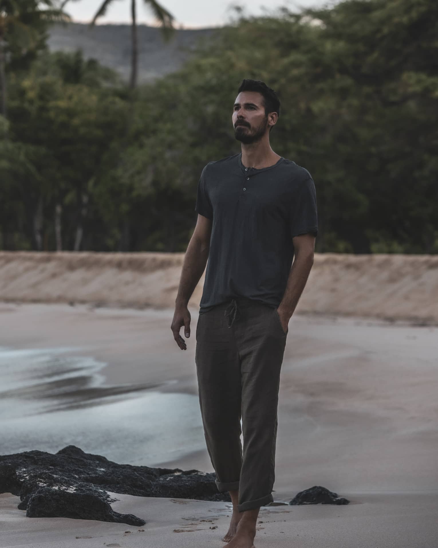 A man walks on a beach in front of a lush tropical forest