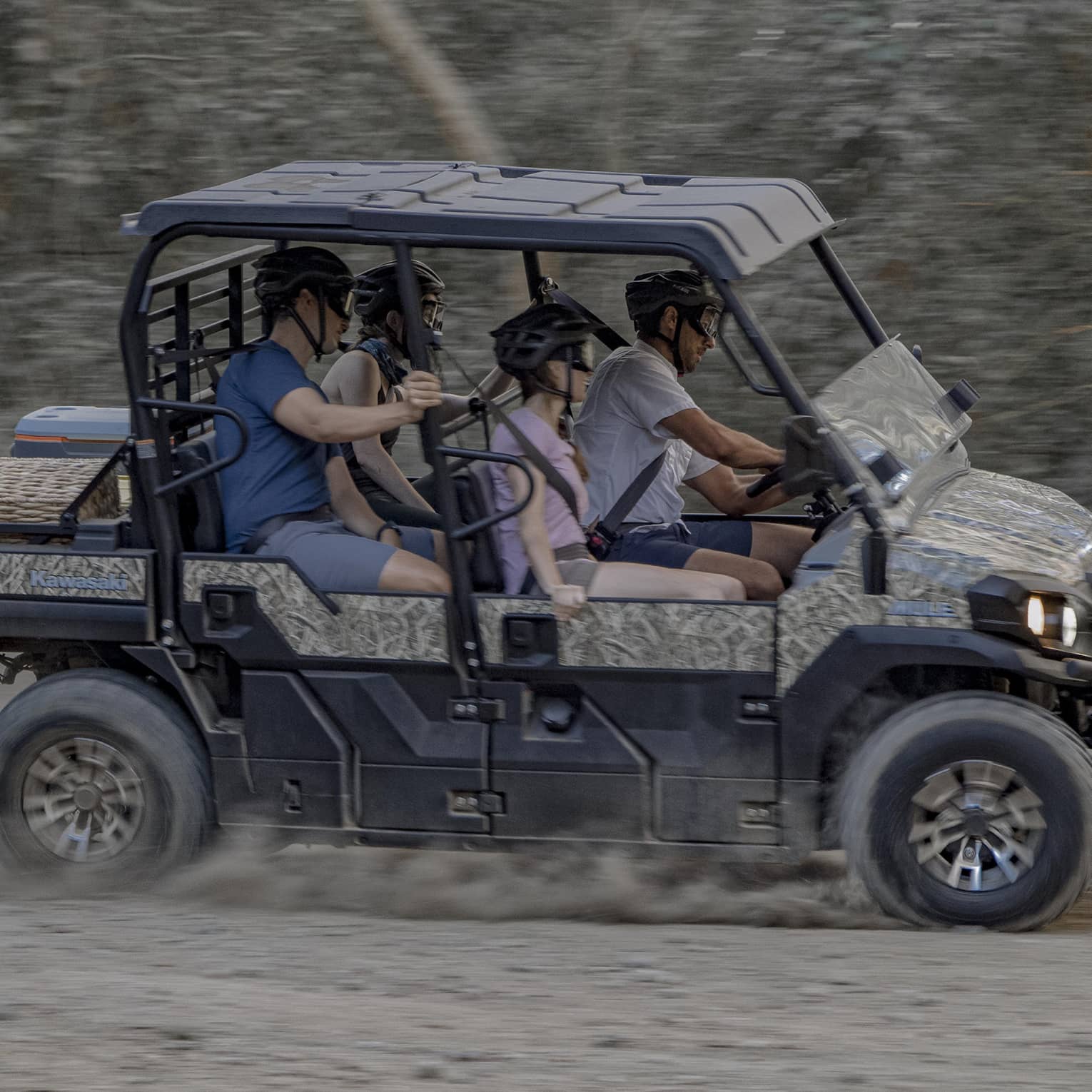 Four people speed along a dirt road in a 4x4 vehicle