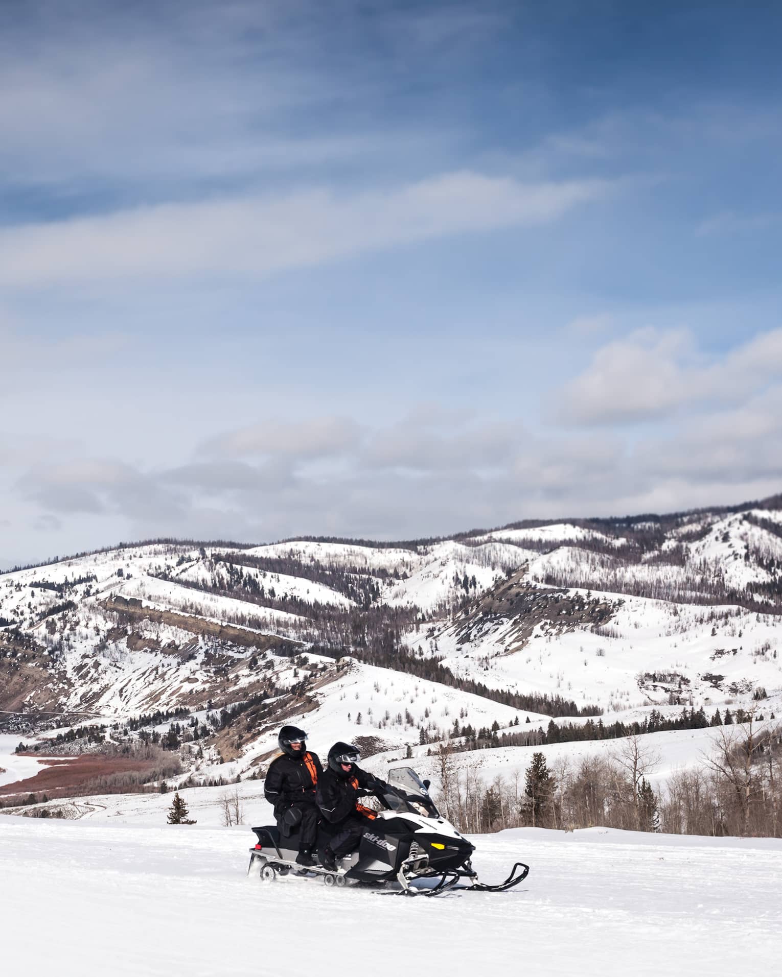 Aerial view of two people riding on a snowmobile in front of snowy mountains