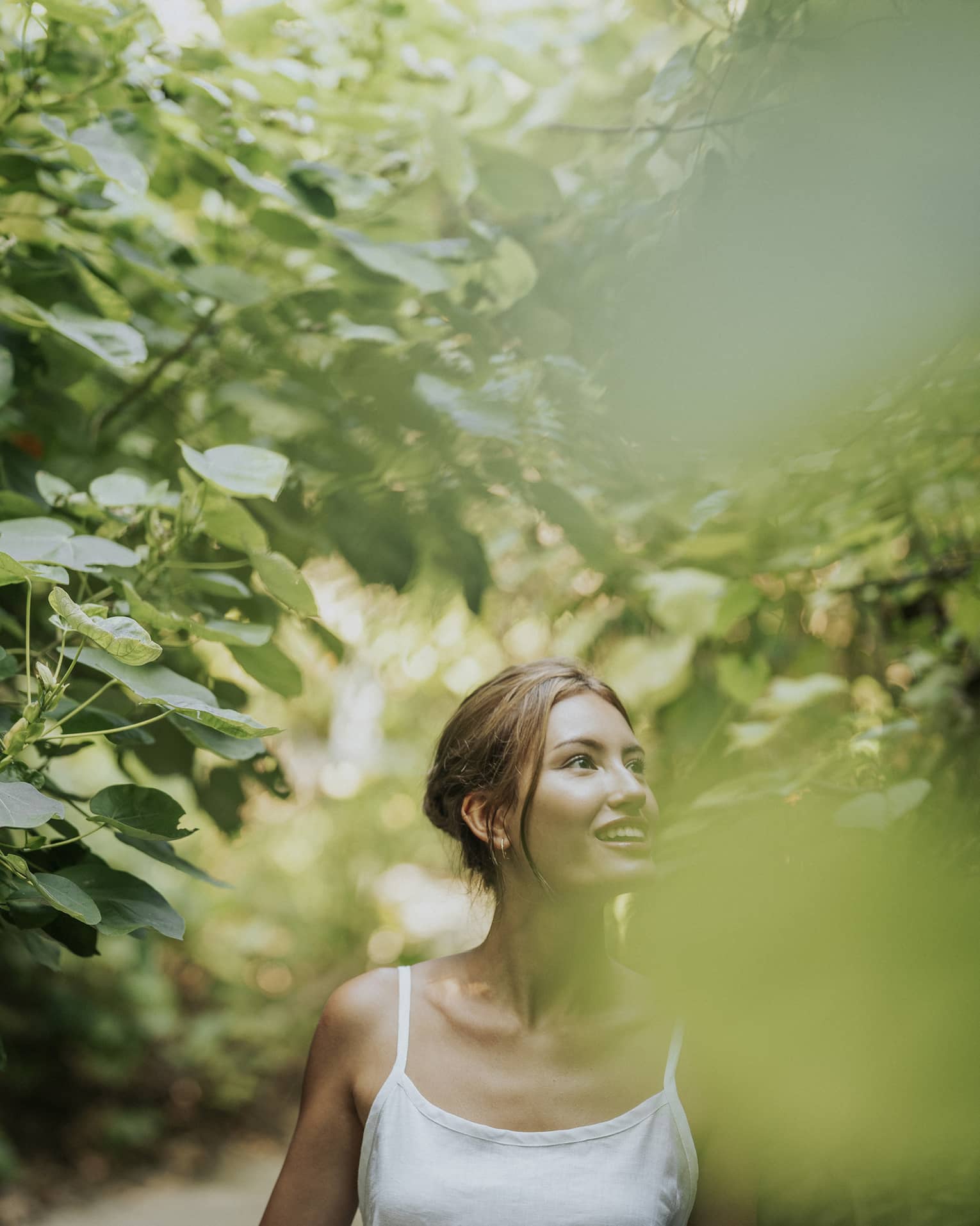 Woman in white tank top walks along heavily tree-lined path