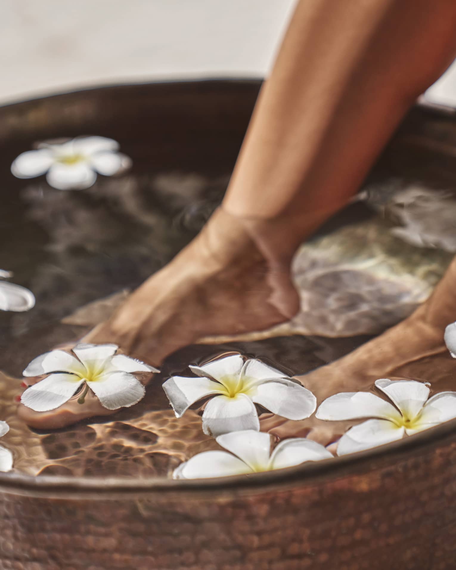 A woman's feet in a bowl of water and flowers.