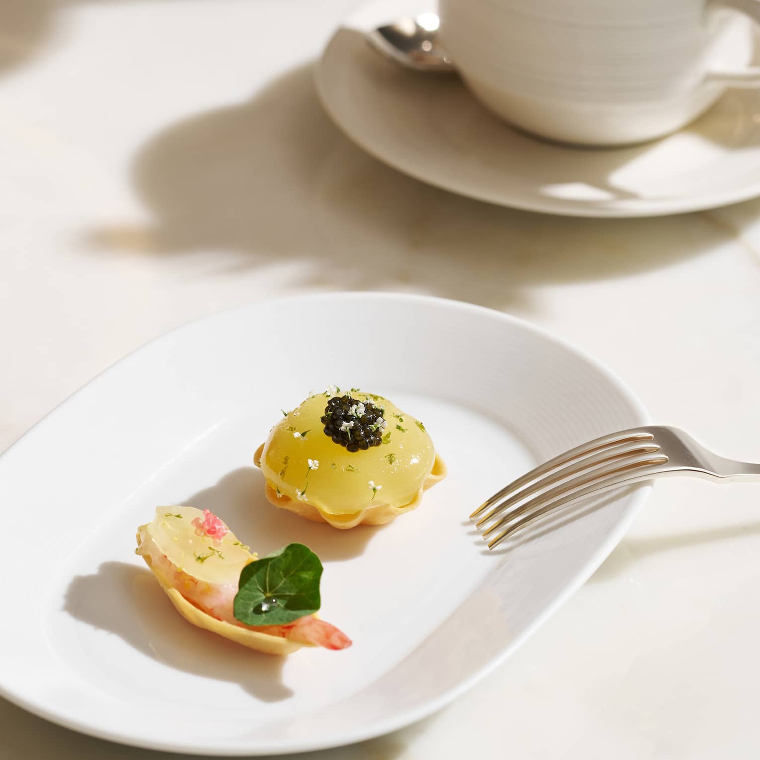 Two colourful pastries on a white plate, with a cup of hot tea in the background