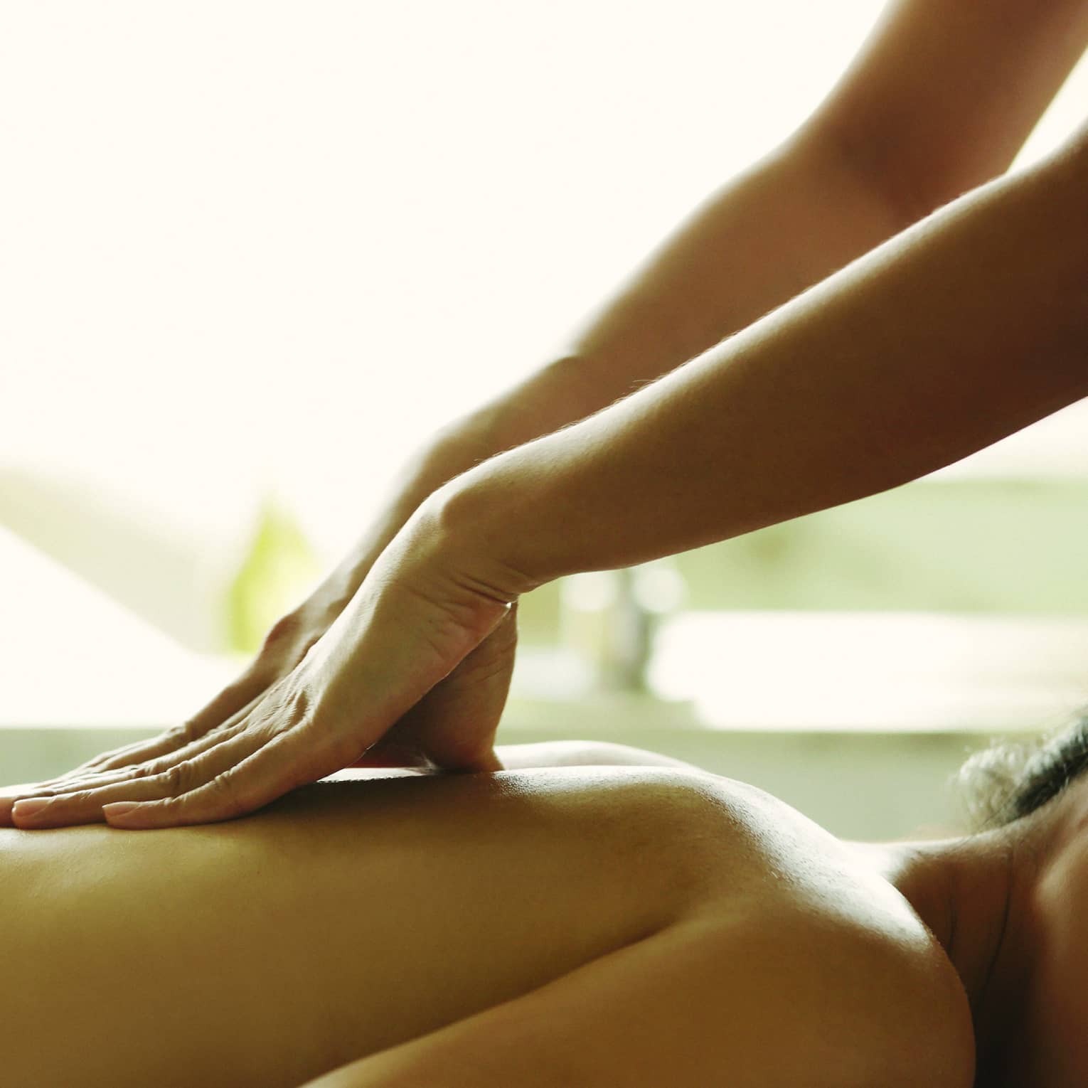 Masseuse reaches over, massages woman's bare back as she lies on spa table