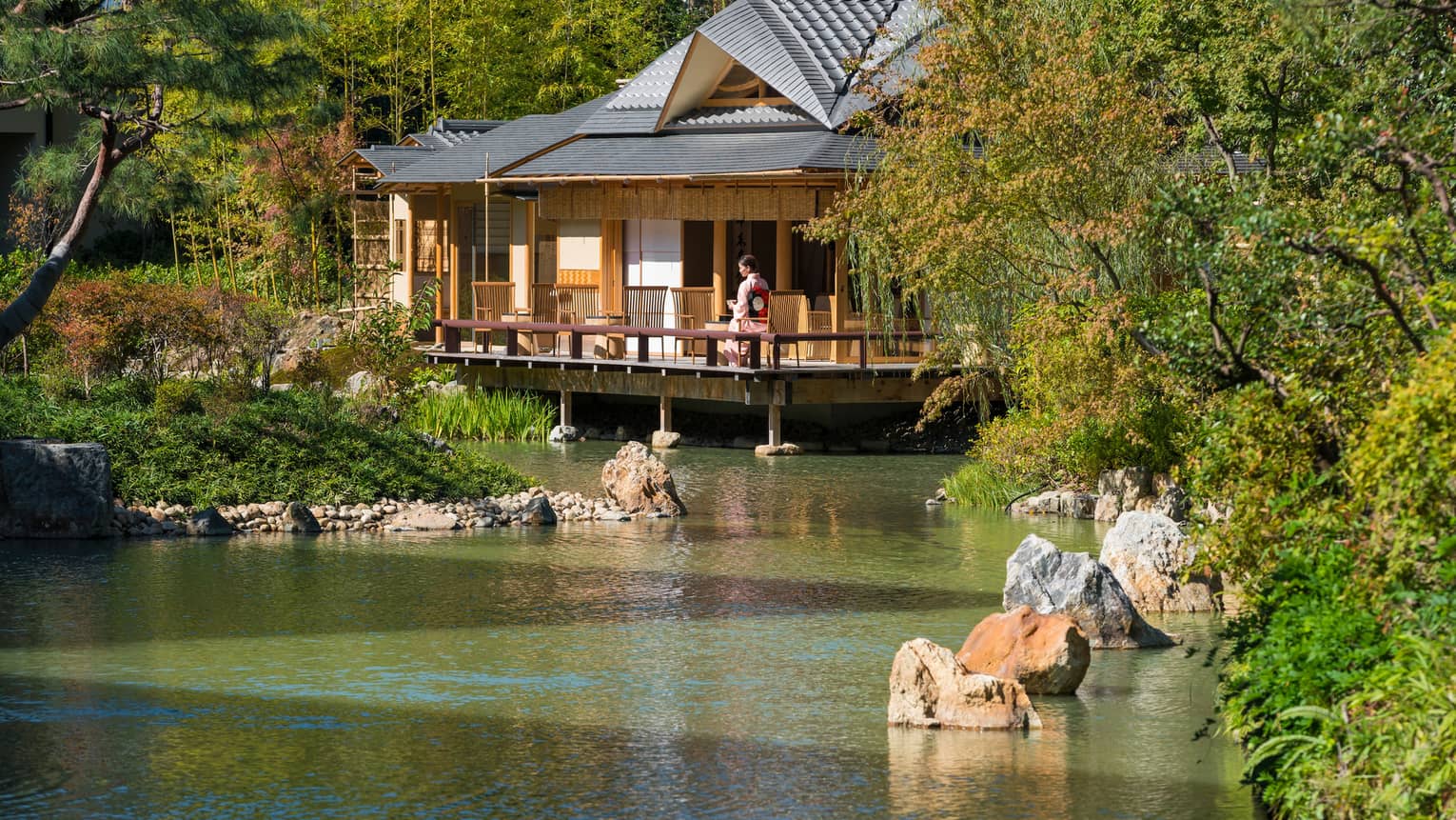 View across pond to bungalow where woman in robe sits on patio