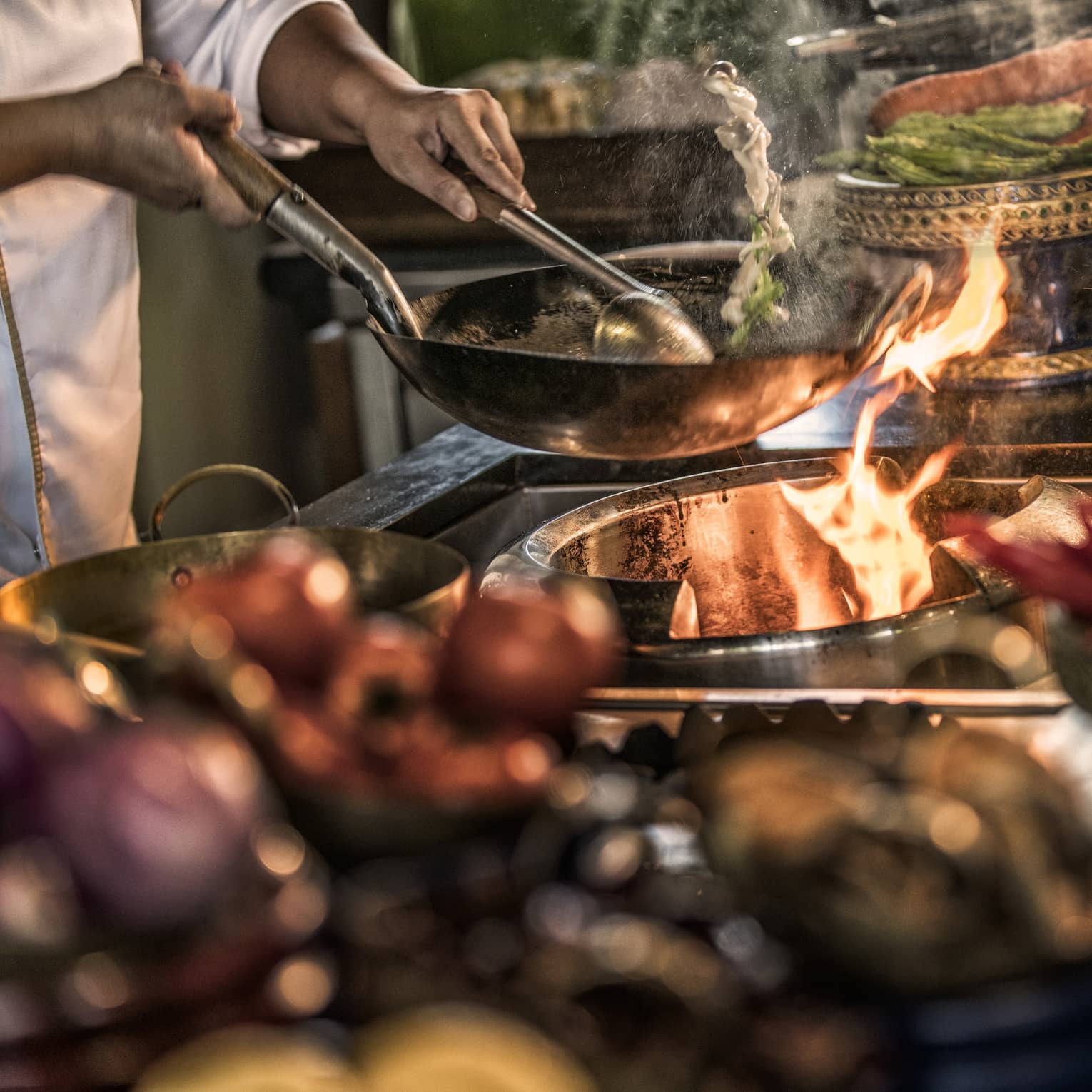 Close-up of chef stirring meals in copper pans over stove, flames