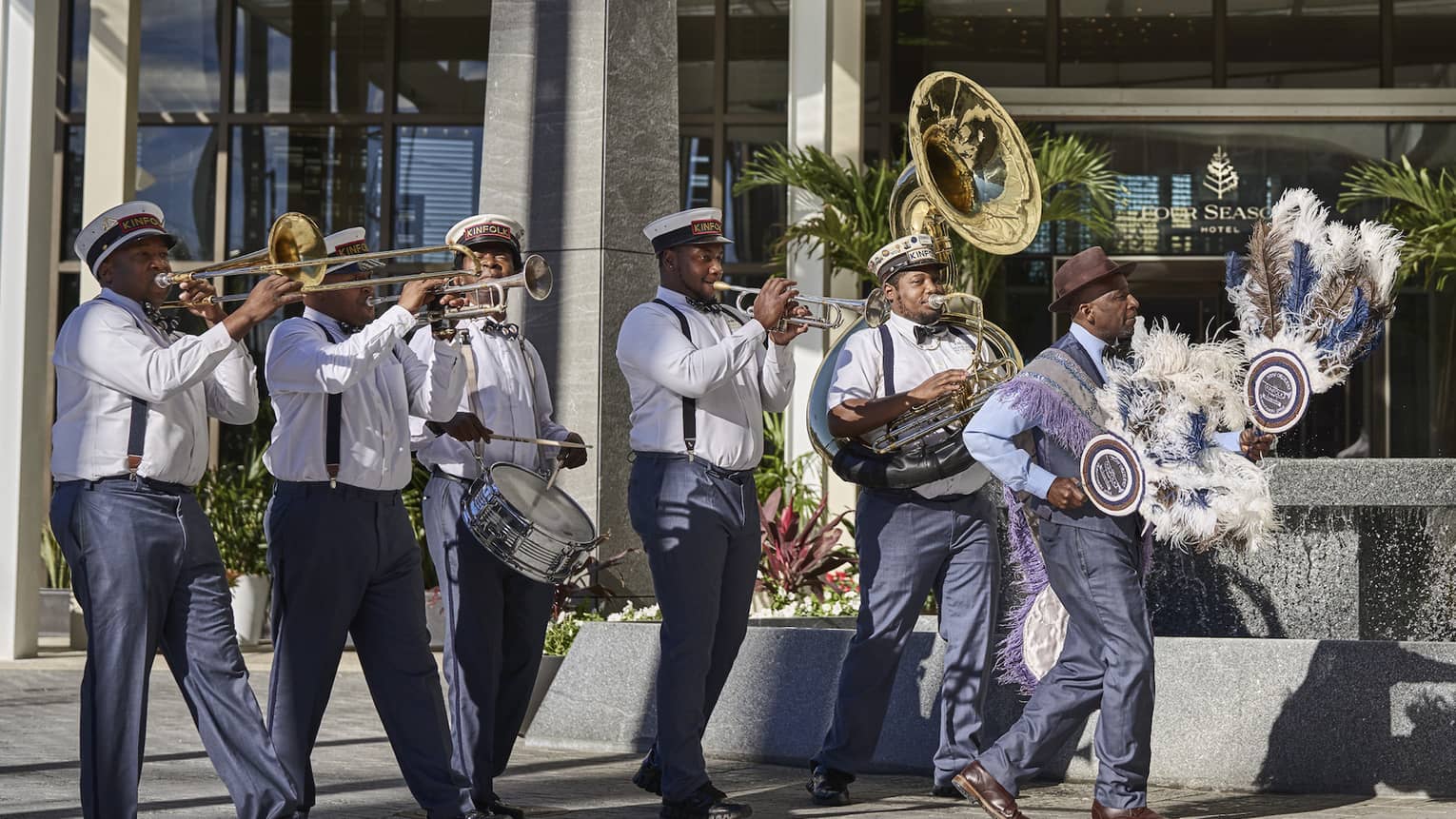 Couple with parasols marches in front of the Hotel, followed by a band
