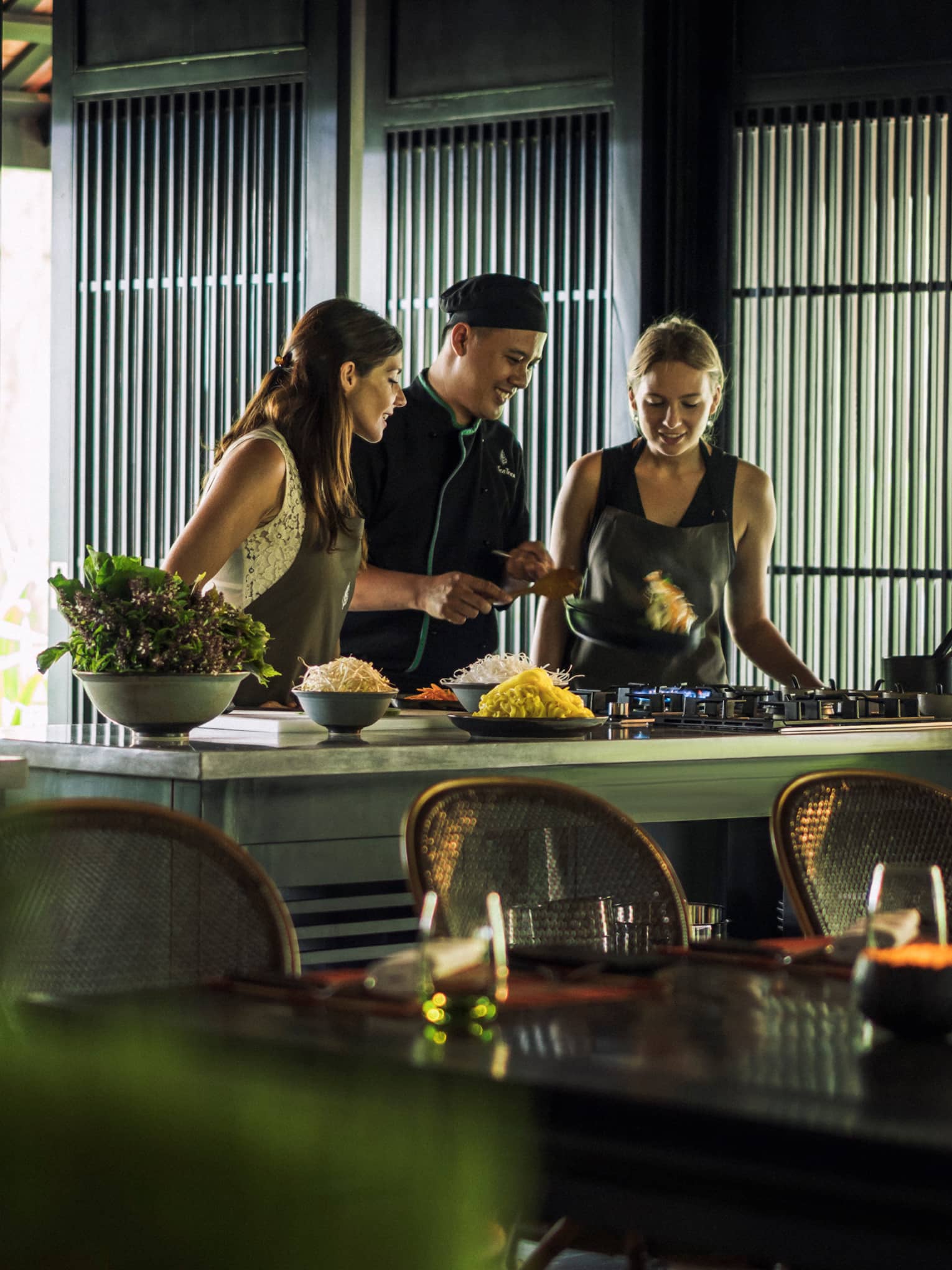 Chef, two women look at pan on kitchen range at Hoi An Cooking Academy 
