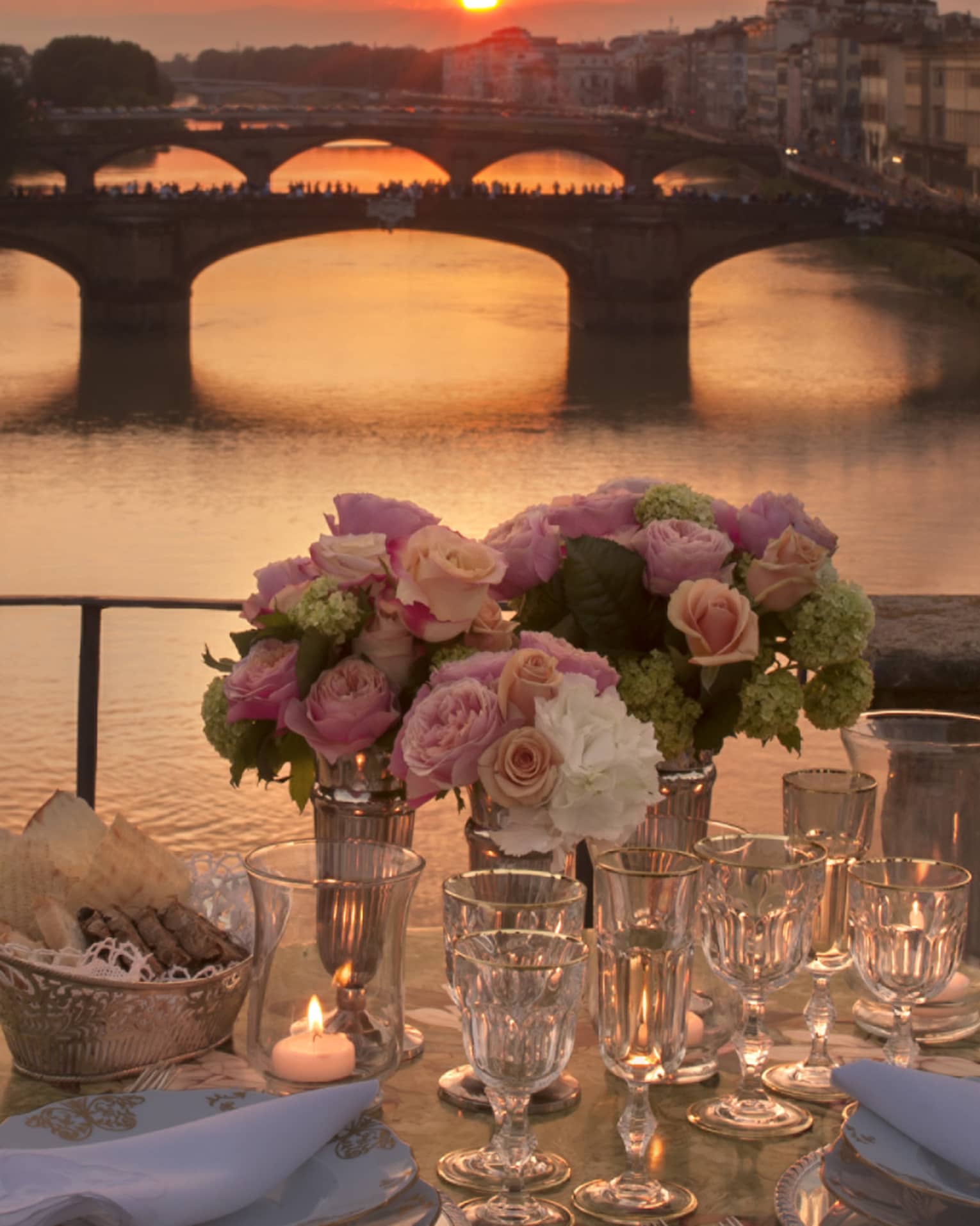 Pink roses in vases on formal dining table on bridge overlooking canal, sunset